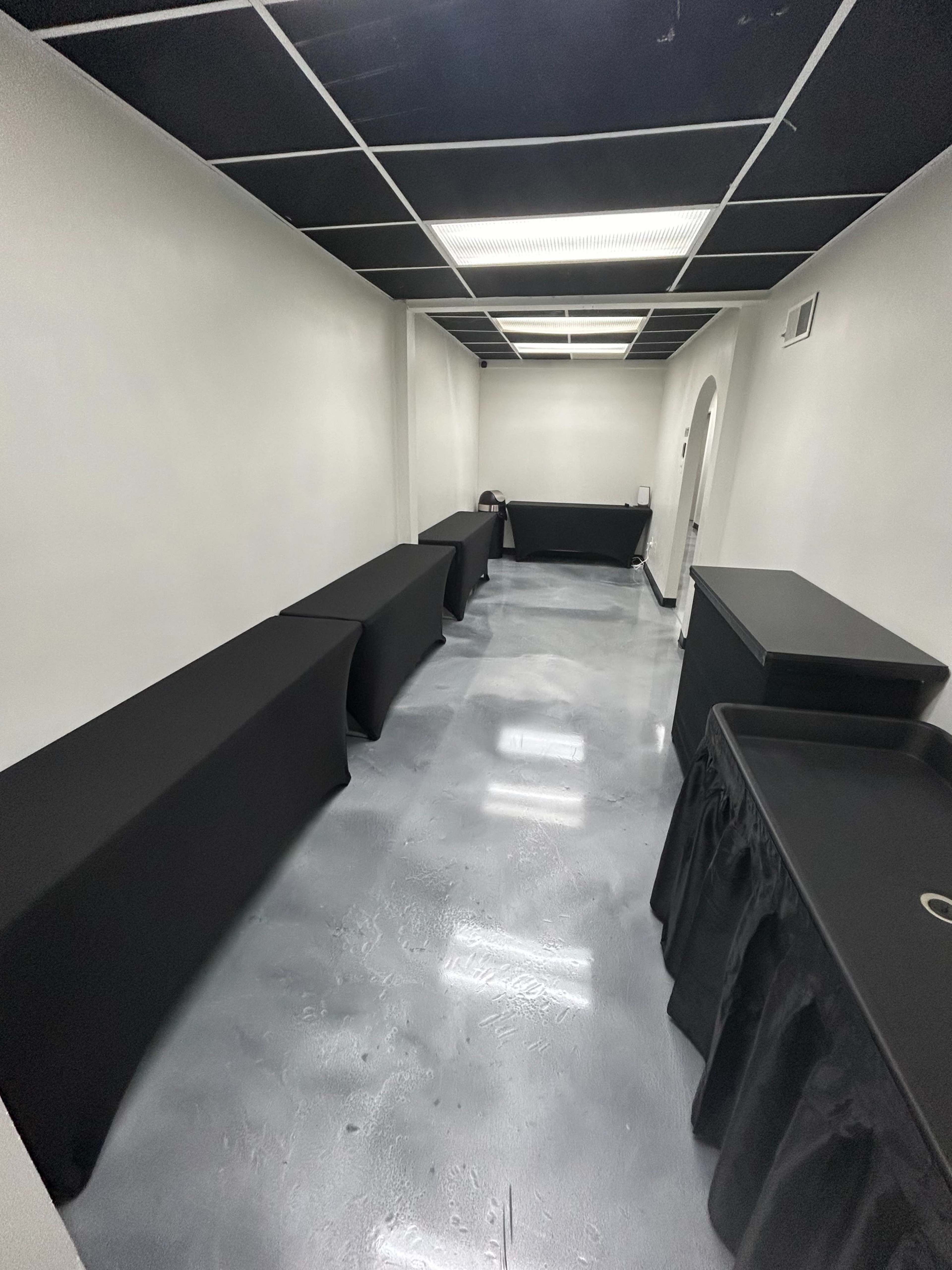 A narrow room with a polished gray floor, featuring several black tables covered with cloth along the side walls.