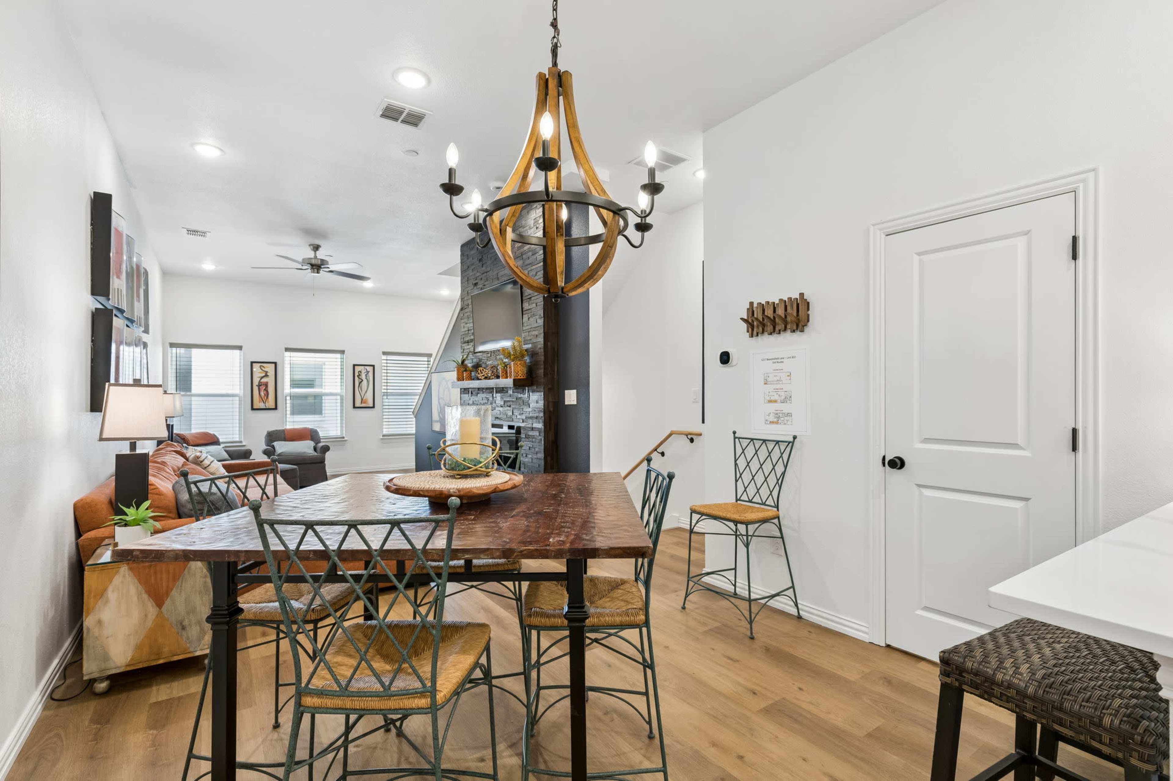 The image shows a modern open-concept living area with a dining table and four chairs, a cozy seating arrangement, and a stone accent wall with a television.