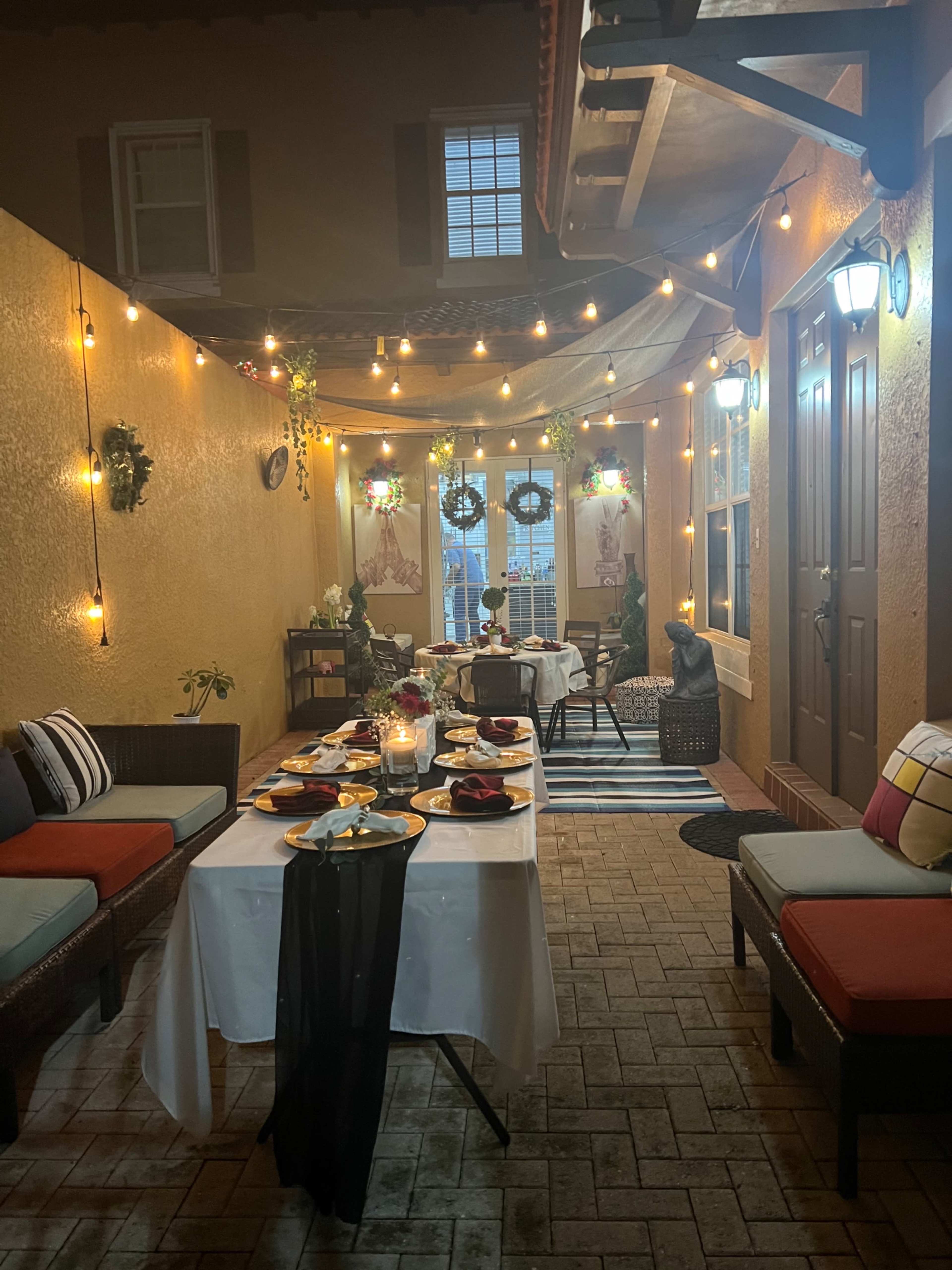A cozy outdoor dining area illuminated with string lights, featuring a table set for a meal and decorative elements against a backdrop of warm-colored walls.