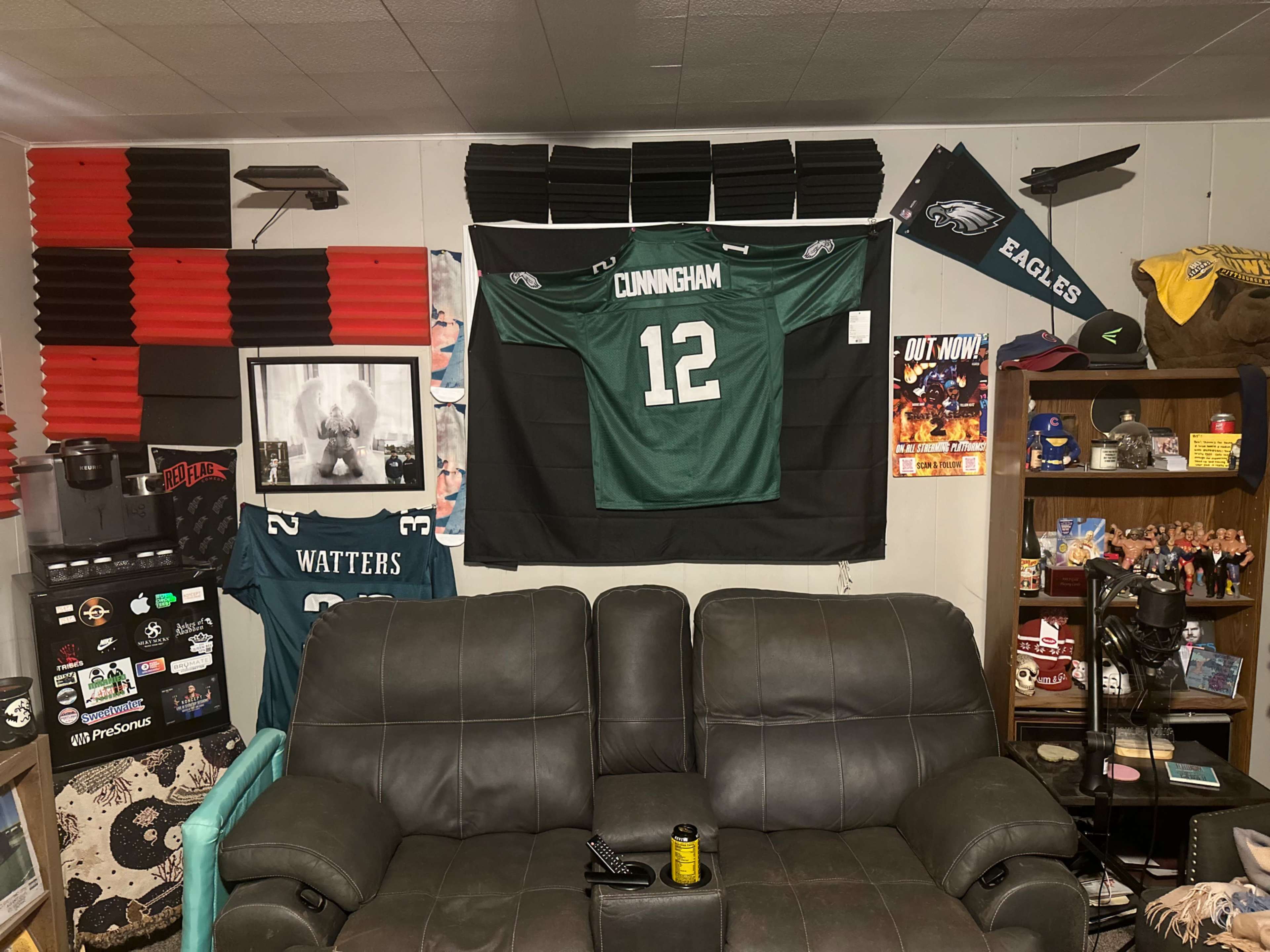 A cozy room with a black couch, sports memorabilia, and an Eagles jersey hanging on the wall.