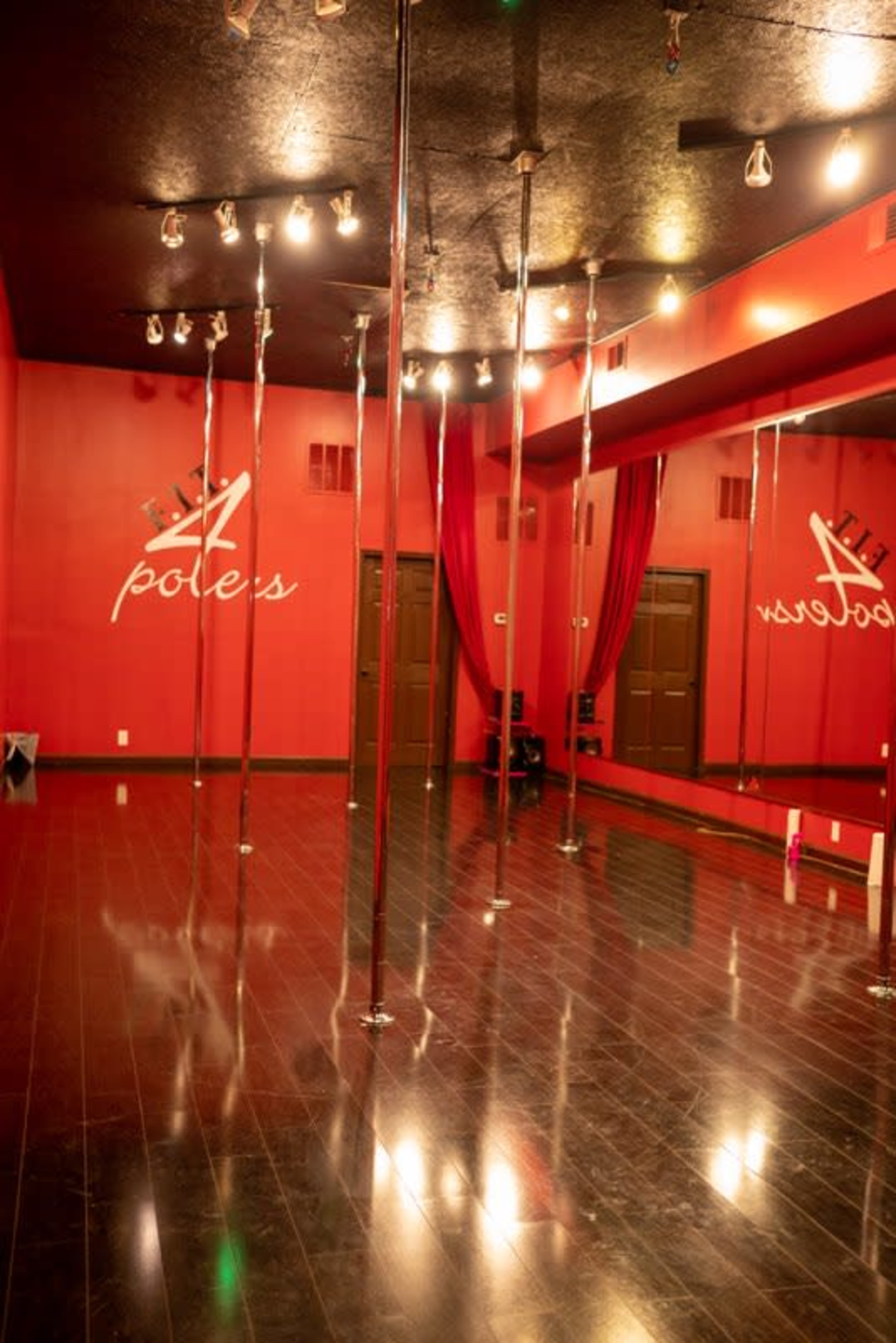 A dance studio with shiny pole fixtures and a red wall featuring the name "A Poles."