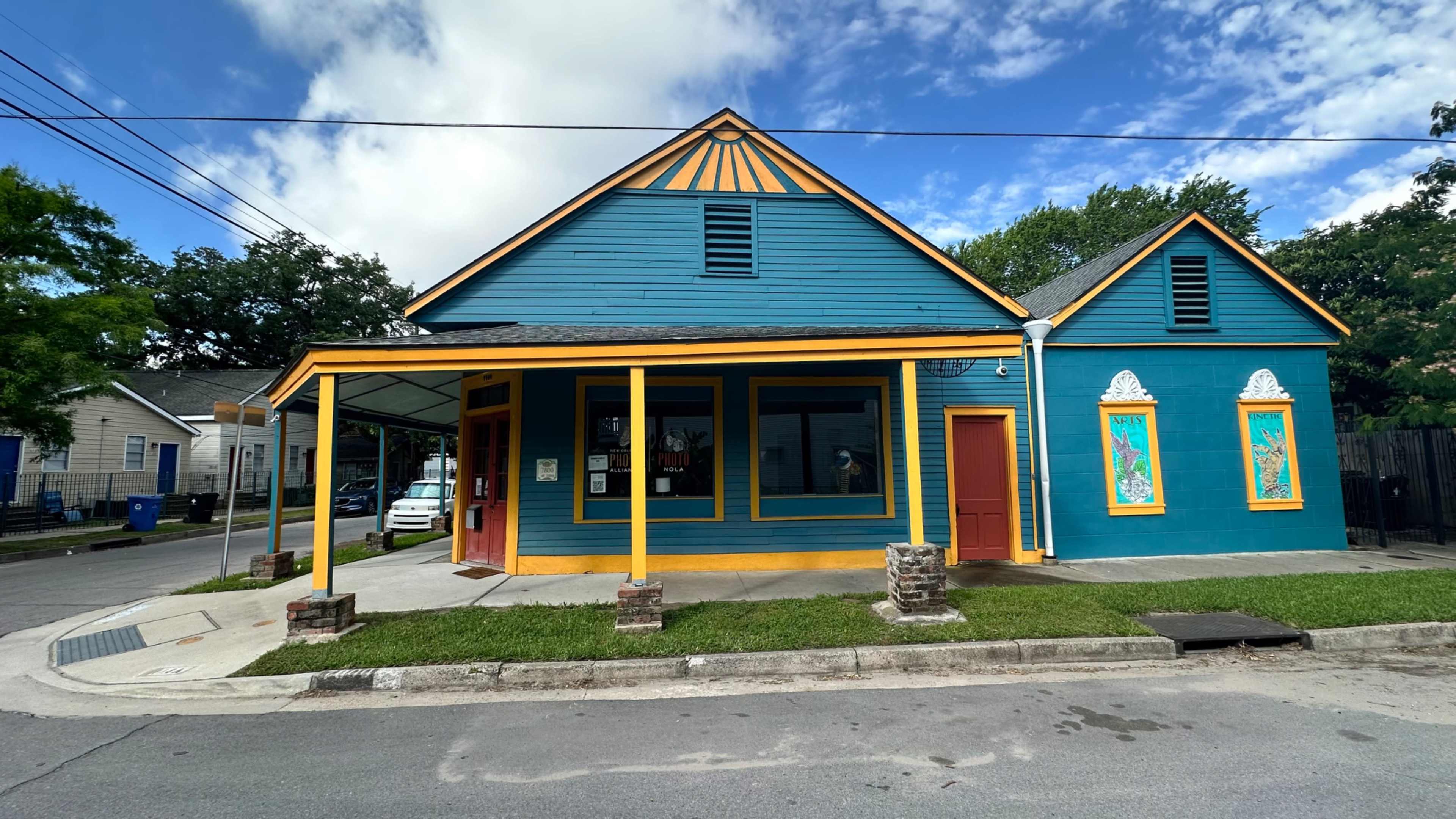 The image shows a brightly colored, two-story house with blue walls and yellow trim on a street corner.