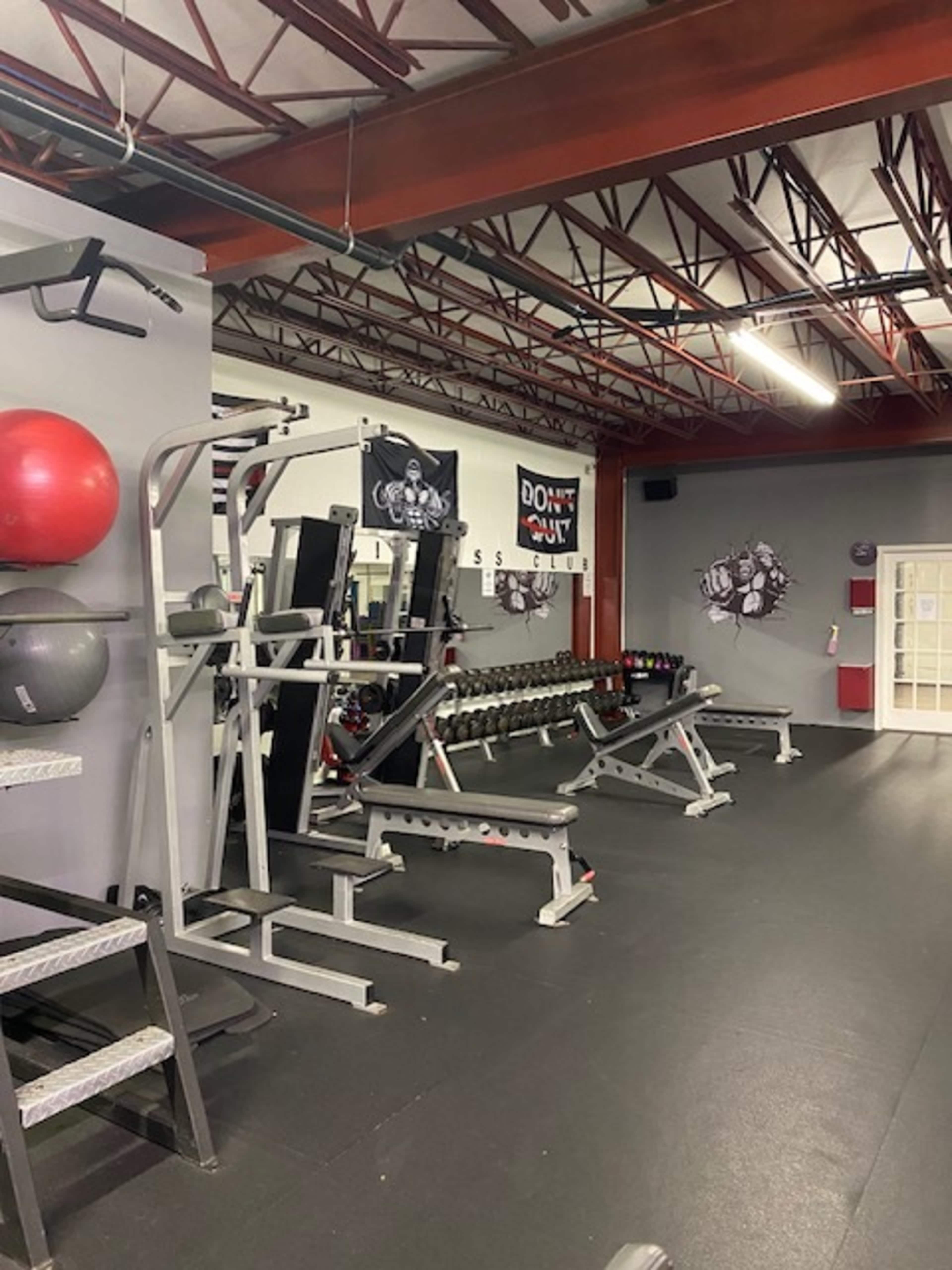 A gym interior with various weight machines, free weights, and exercise equipment arranged along a wall.