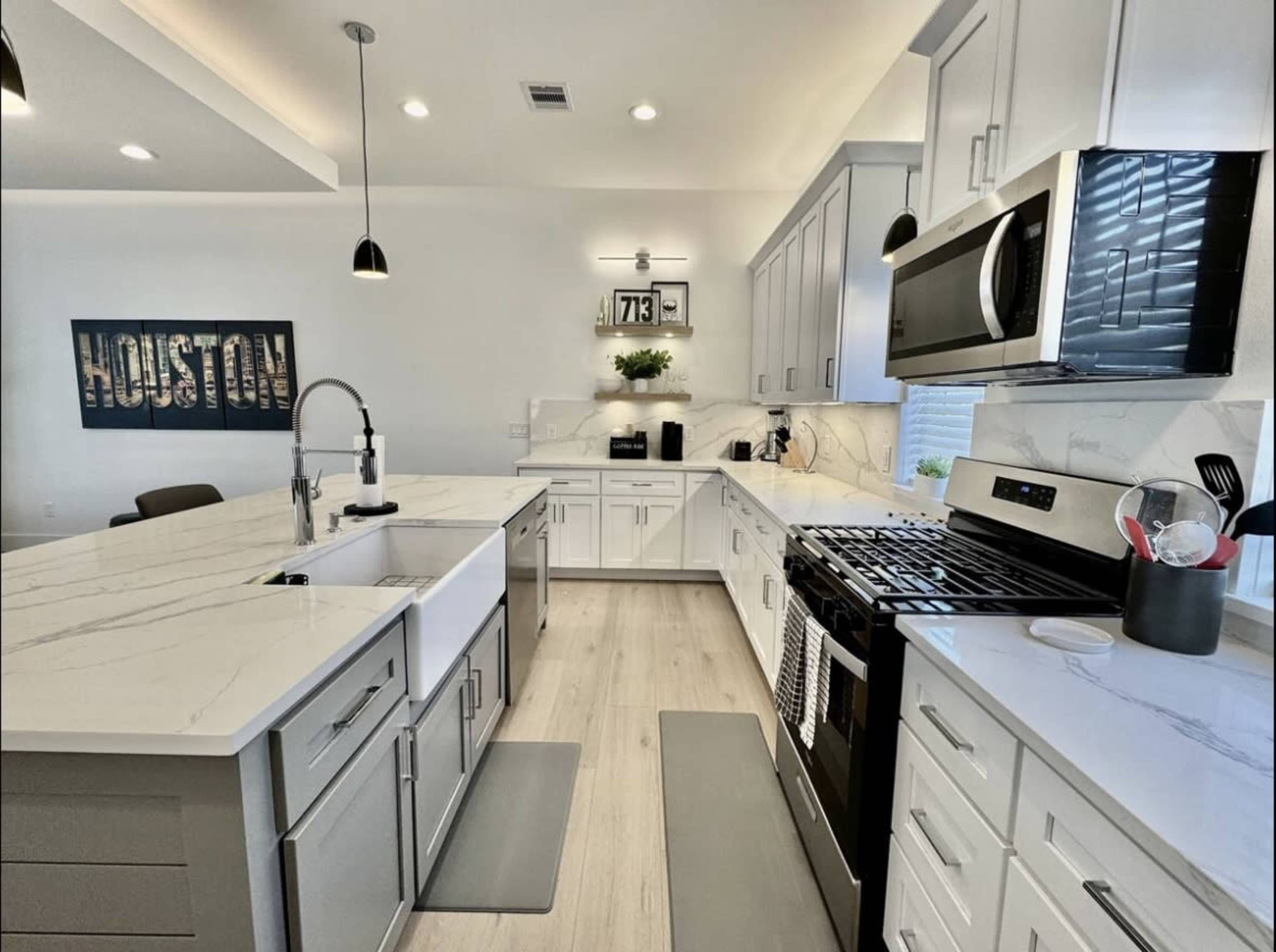 The kitchen features white cabinets, marble countertops, stainless steel appliances, and a double sink, with a sign on the wall that reads "HOUSTON."