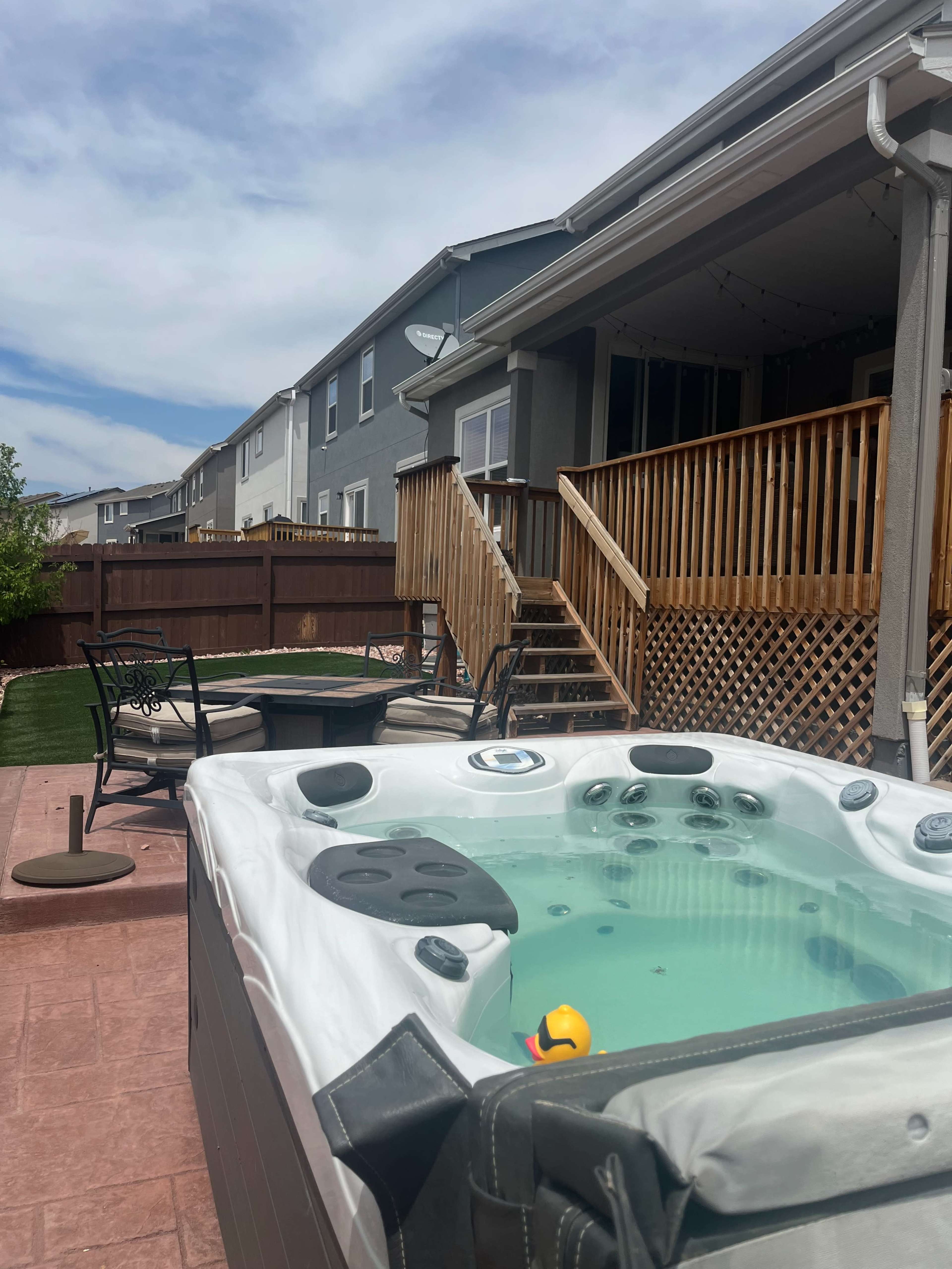 The image shows a backyard with a hot tub, a seating area, and a staircase leading to a house.