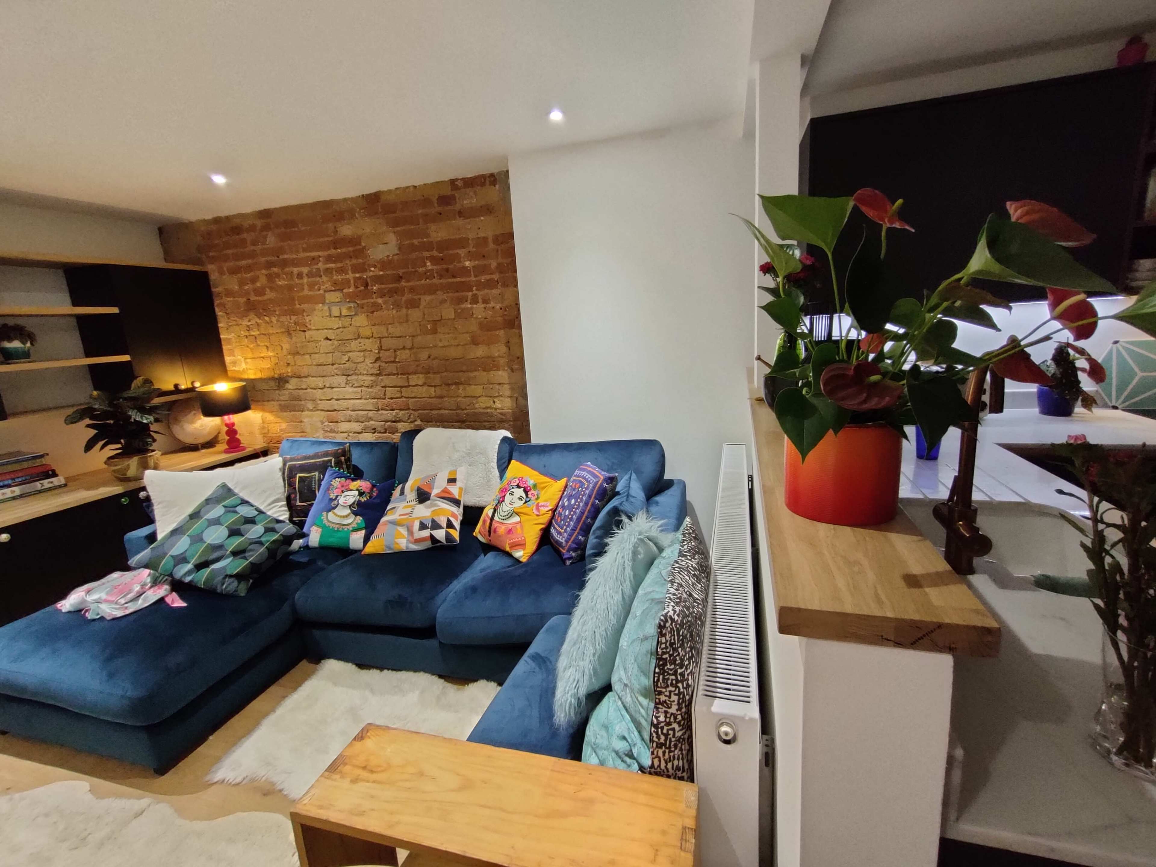 A cozy living room featuring a blue sectional sofa adorned with colorful cushions, a decorative wooden table, and a potted plant on a nearby surface.