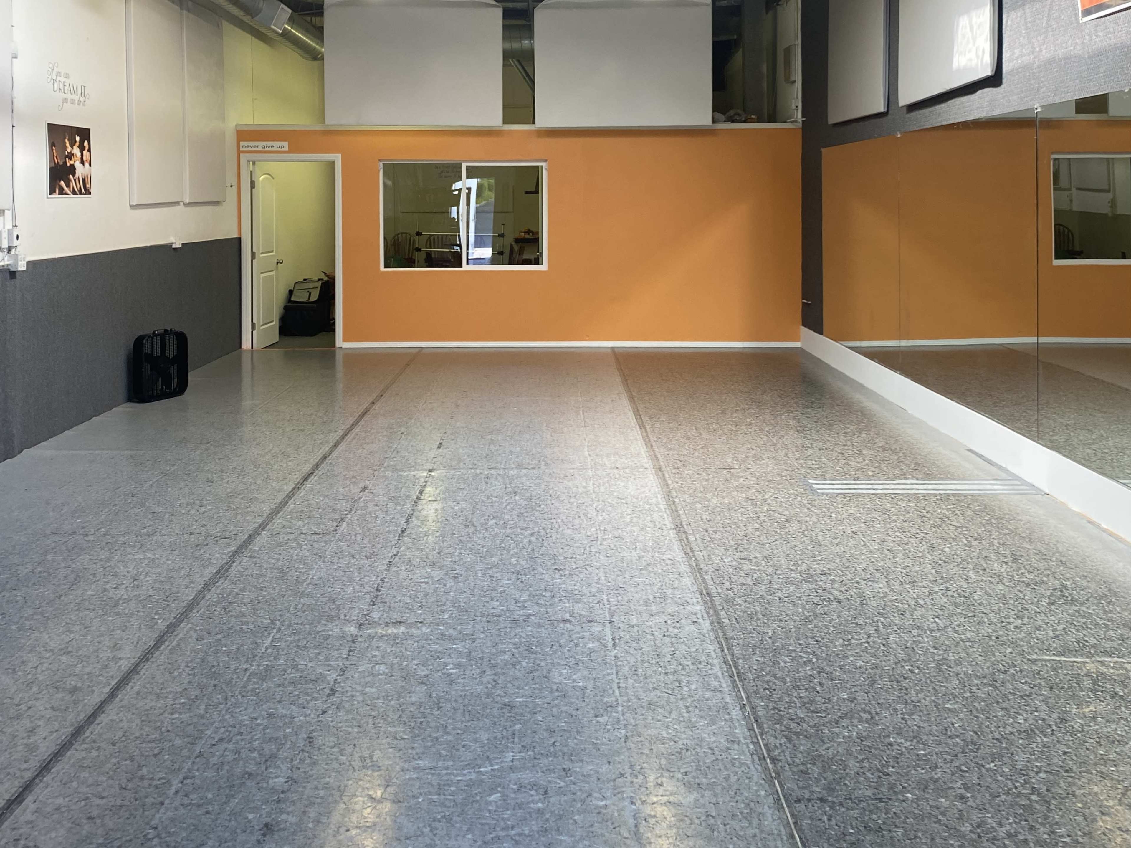 The image shows an empty dance studio with a gray floor, orange and white walls, and large mirrors along one side.