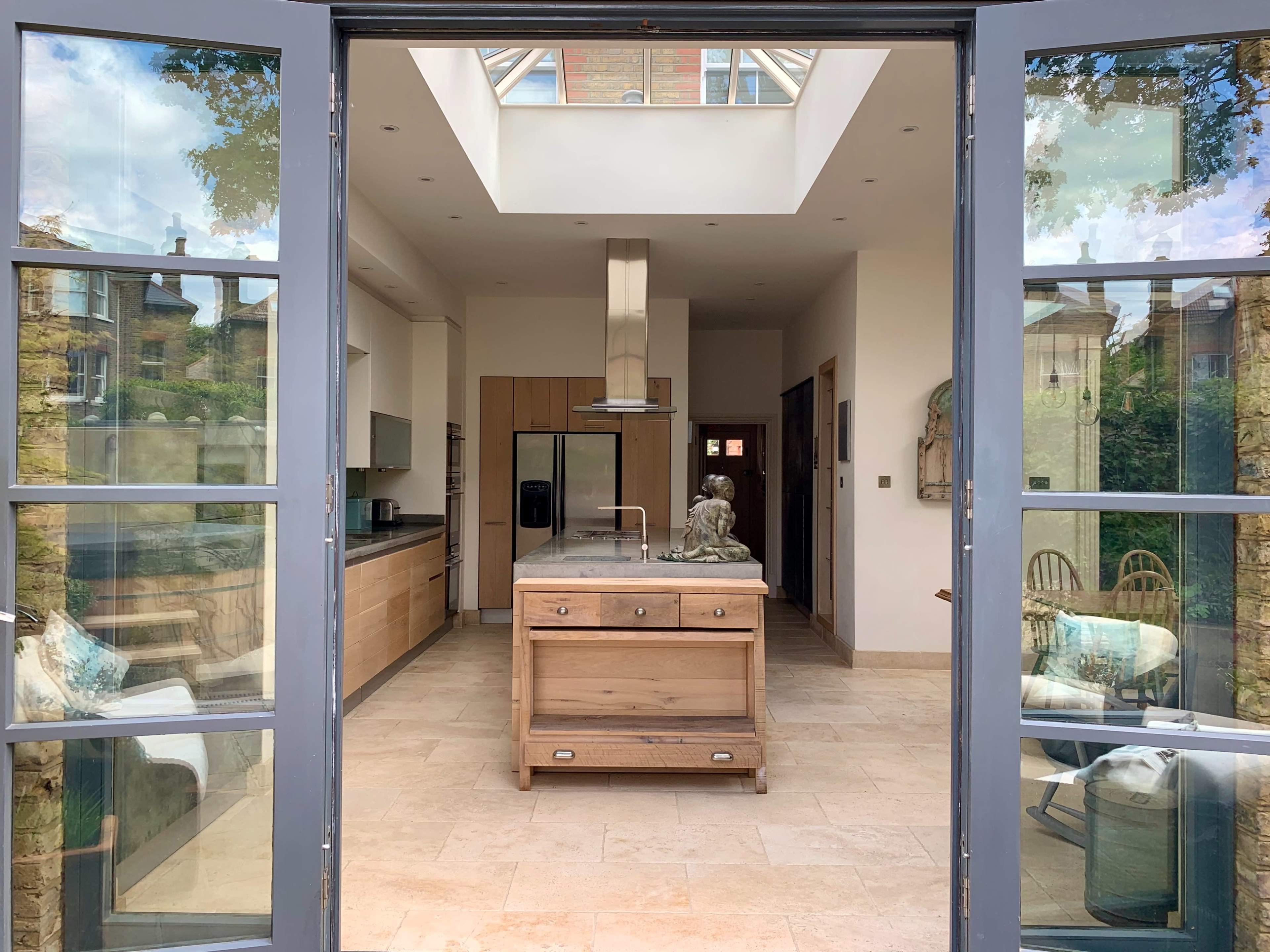 The image shows a spacious kitchen with a central island and large glass doors leading to an outdoor area.