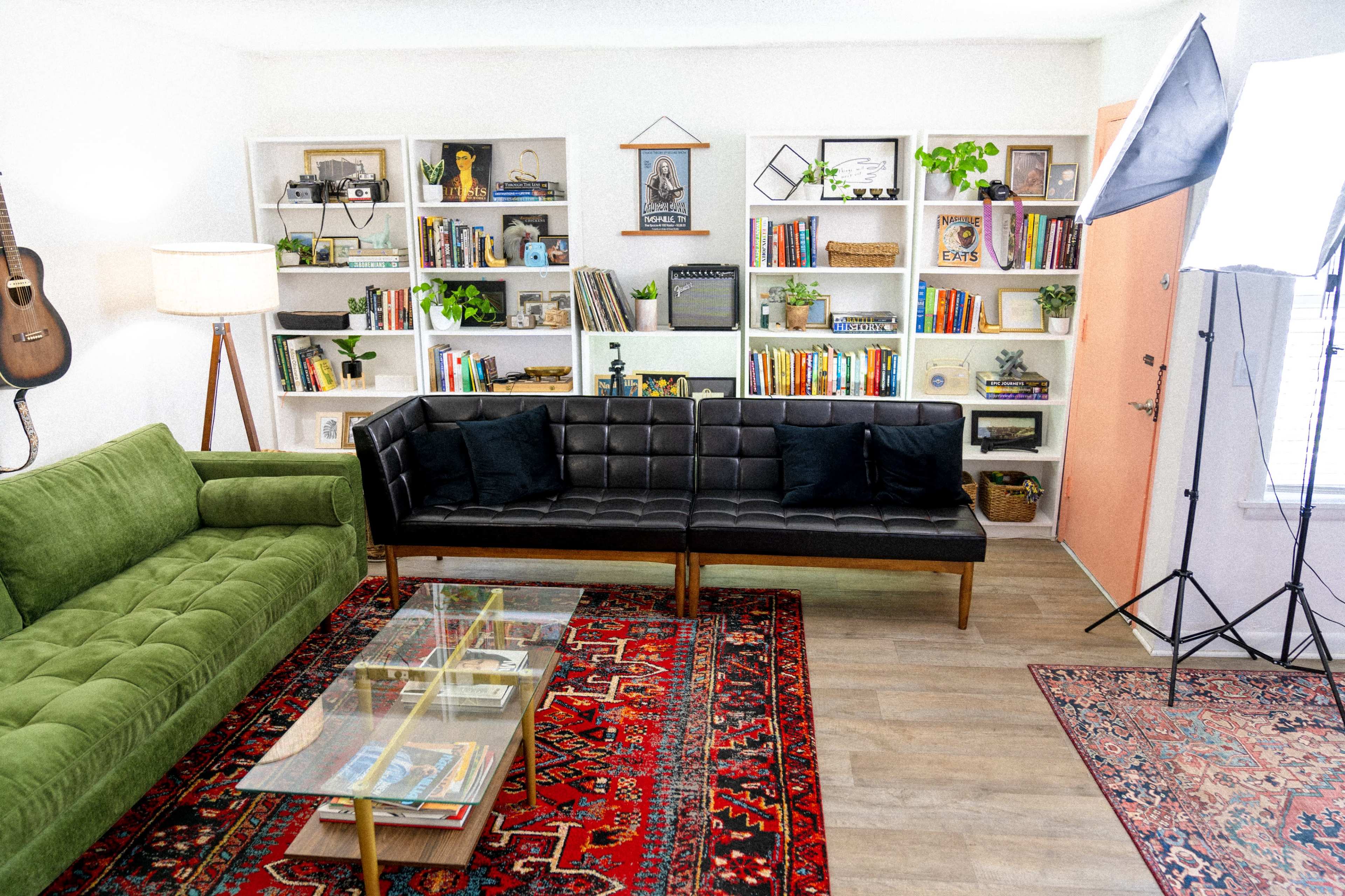 A living room with a green couch, a black leather sofa, a coffee table, and bookshelves filled with books and decorative items.