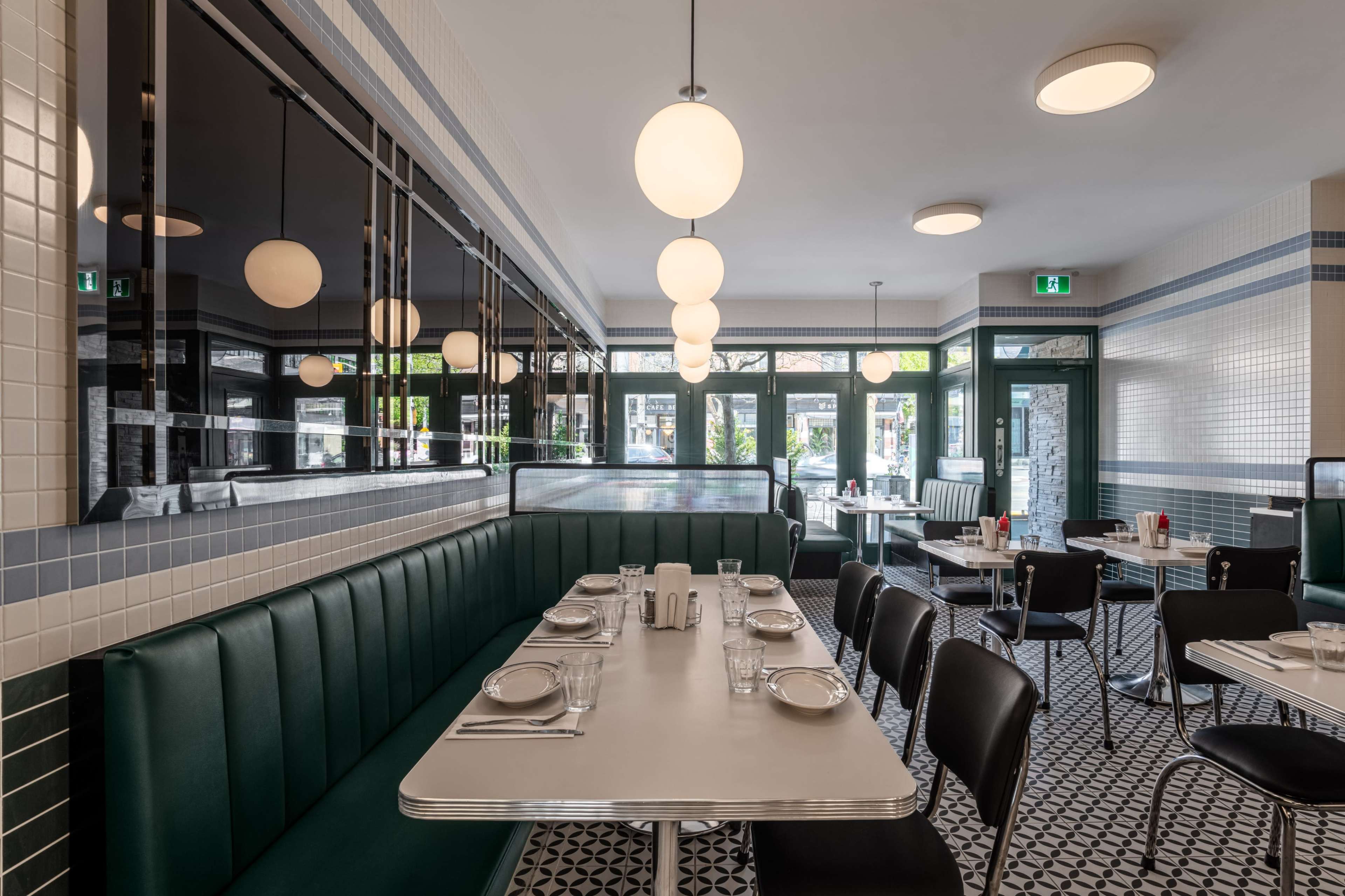 The image shows a modern diner interior with green booths, black chairs, and round pendant lights, featuring tiled walls and a checkered floor.