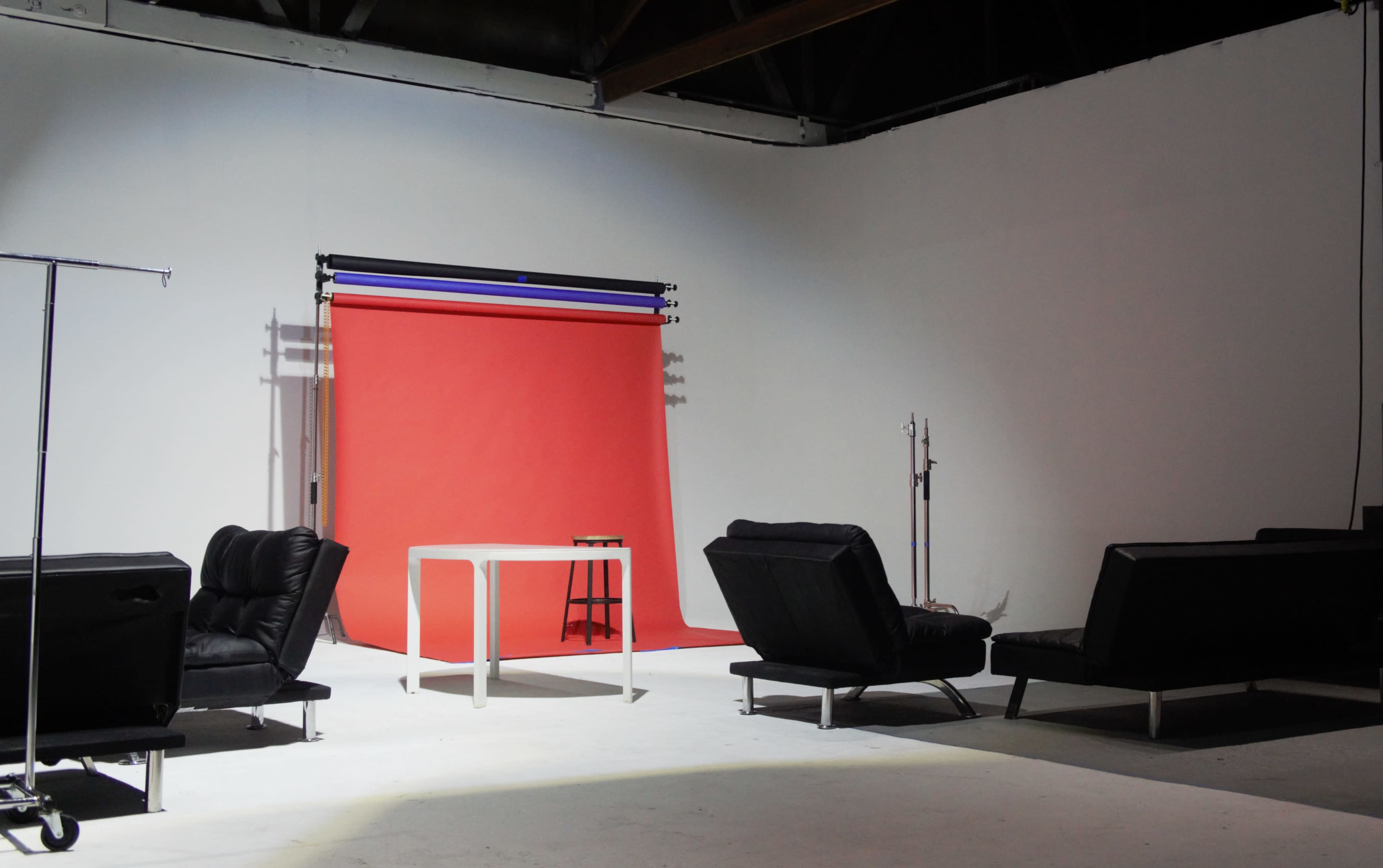 A photo studio features a red backdrop with a table and two black couches arranged around a minimalist space.