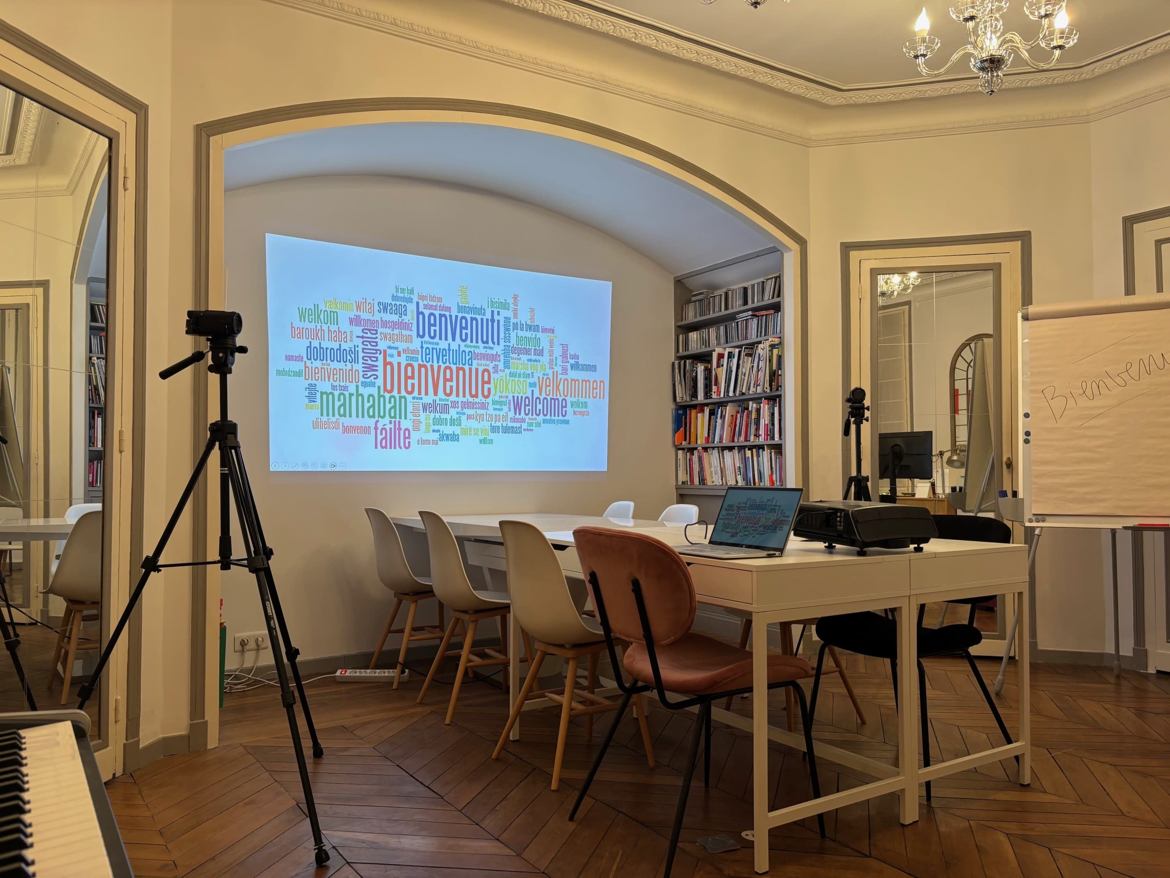 A conference room features a large word cloud display on the wall, surrounded by a table and chairs, with notebooks and cameras set up for a meeting.