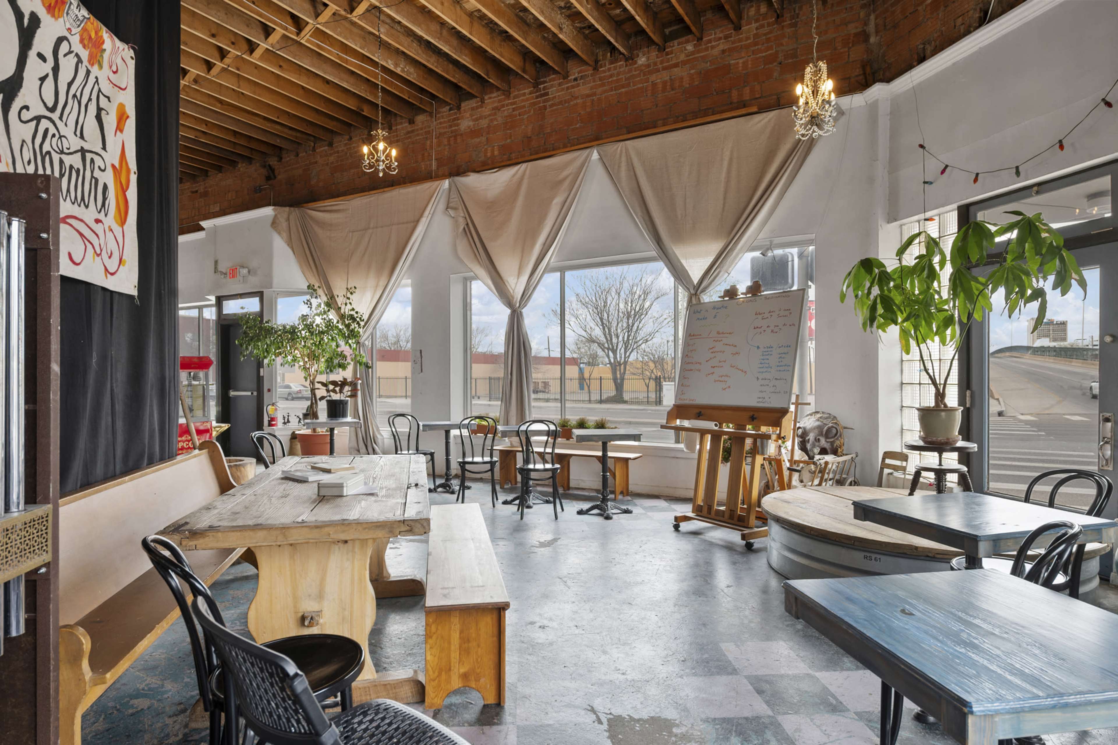 A spacious, well-lit café with wooden tables and chairs, large windows, and a whiteboard on an easel.