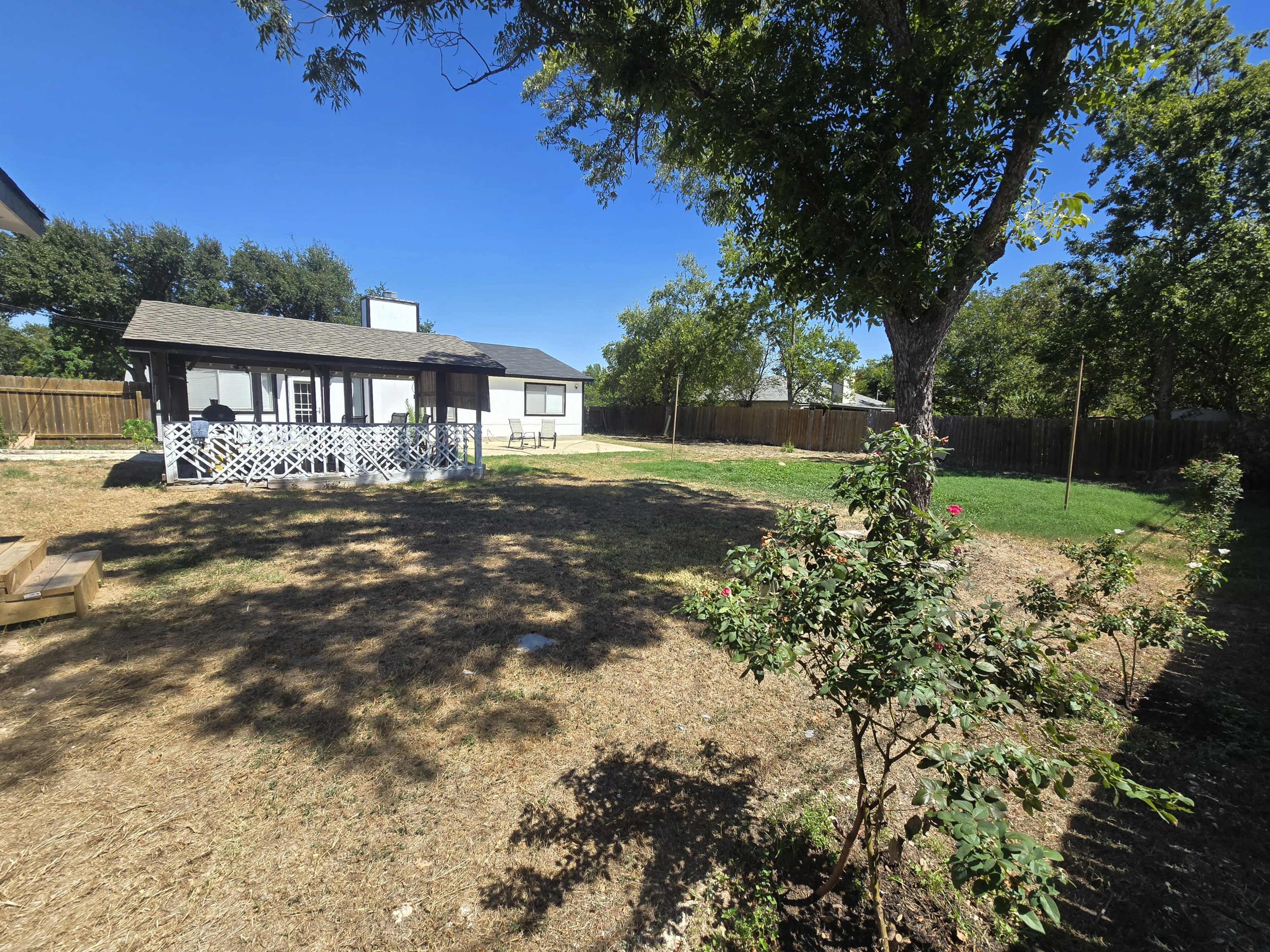 The image shows a spacious backyard with a gazebo, a few trees, and grassy areas under a clear blue sky.