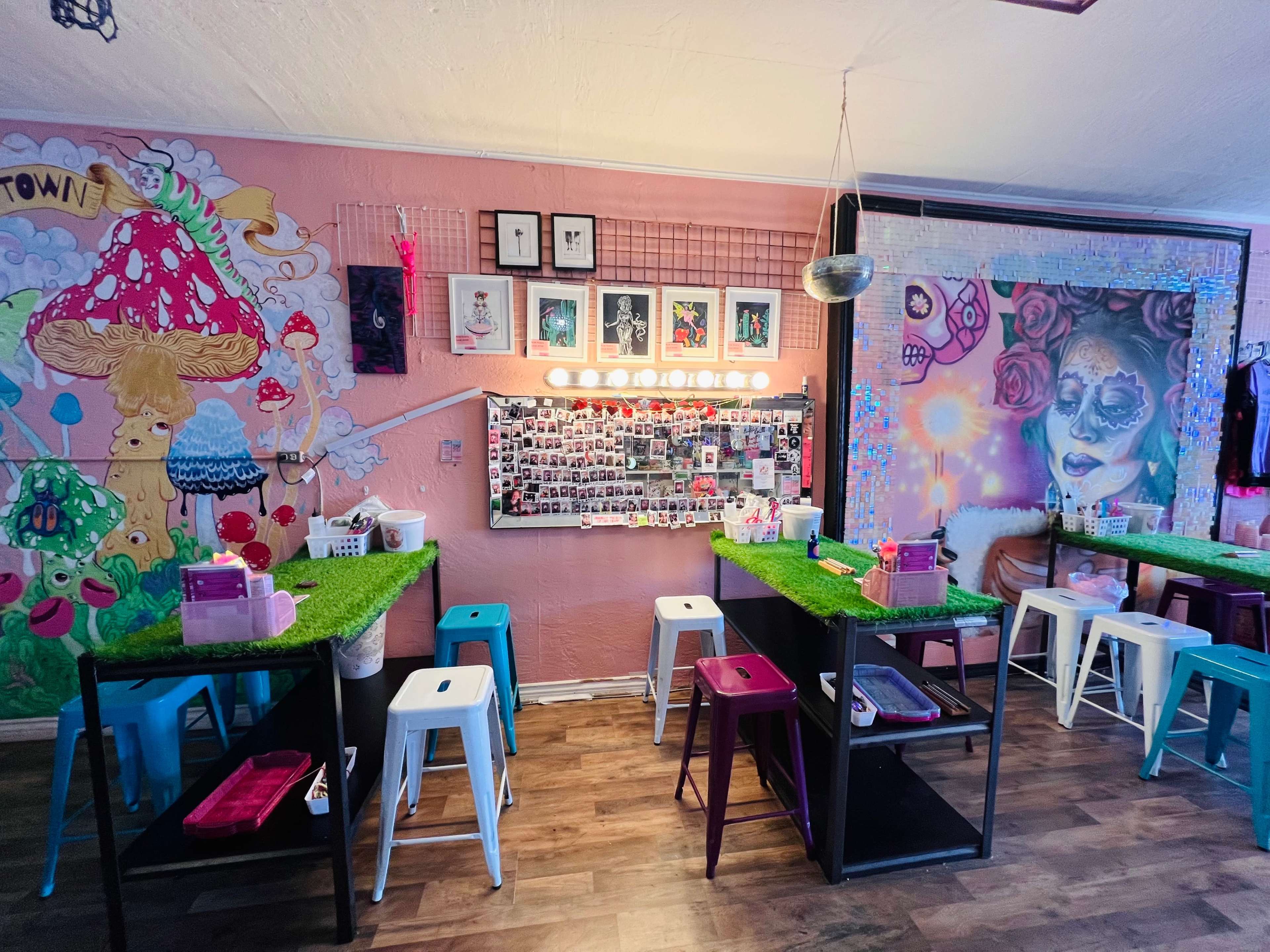 A colorful craft room with tables adorned with grass-like mats, a wall of framed photos, and vibrant murals.