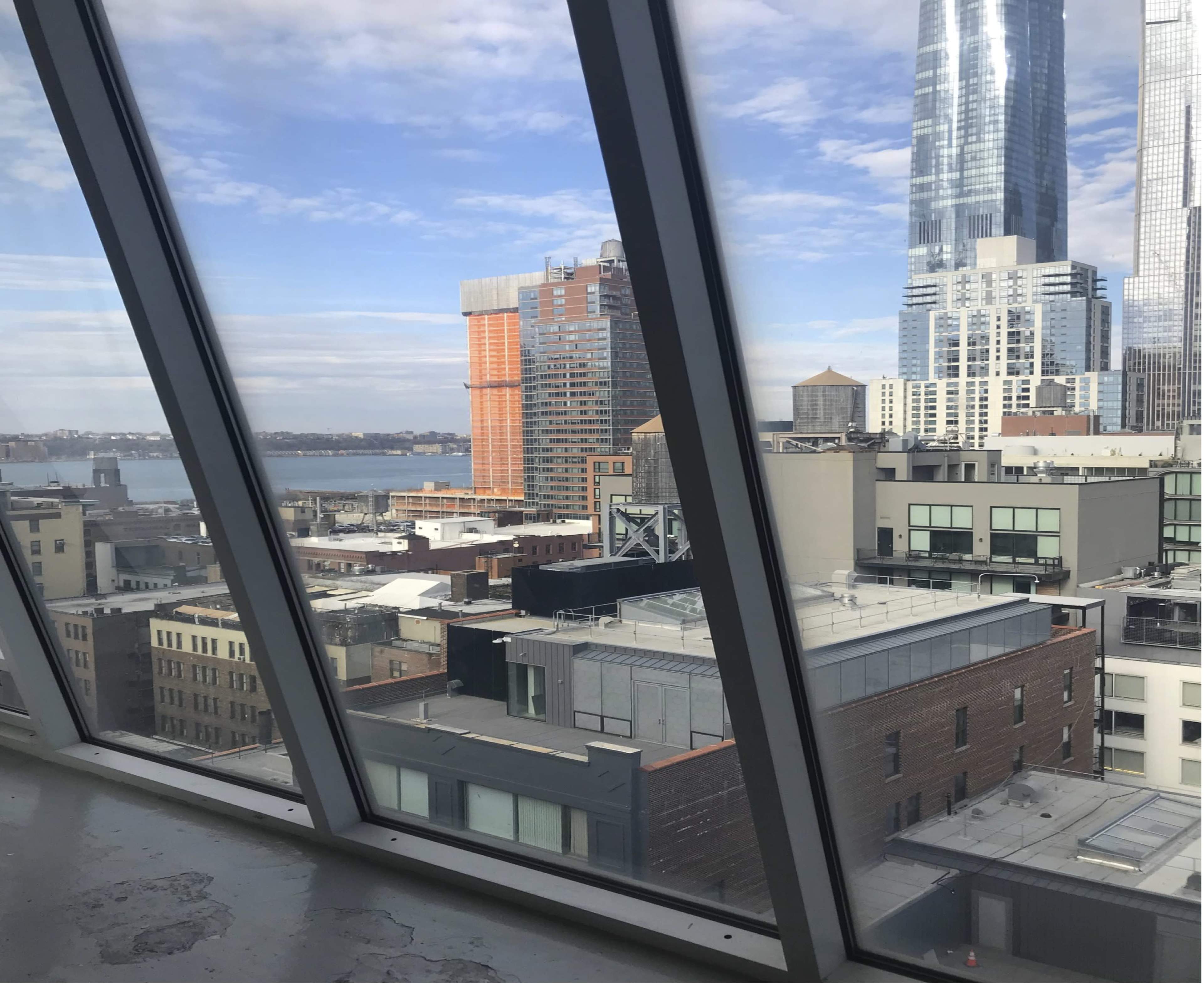 A view through large, angled windows overlooking a cityscape with various buildings and a body of water in the background.