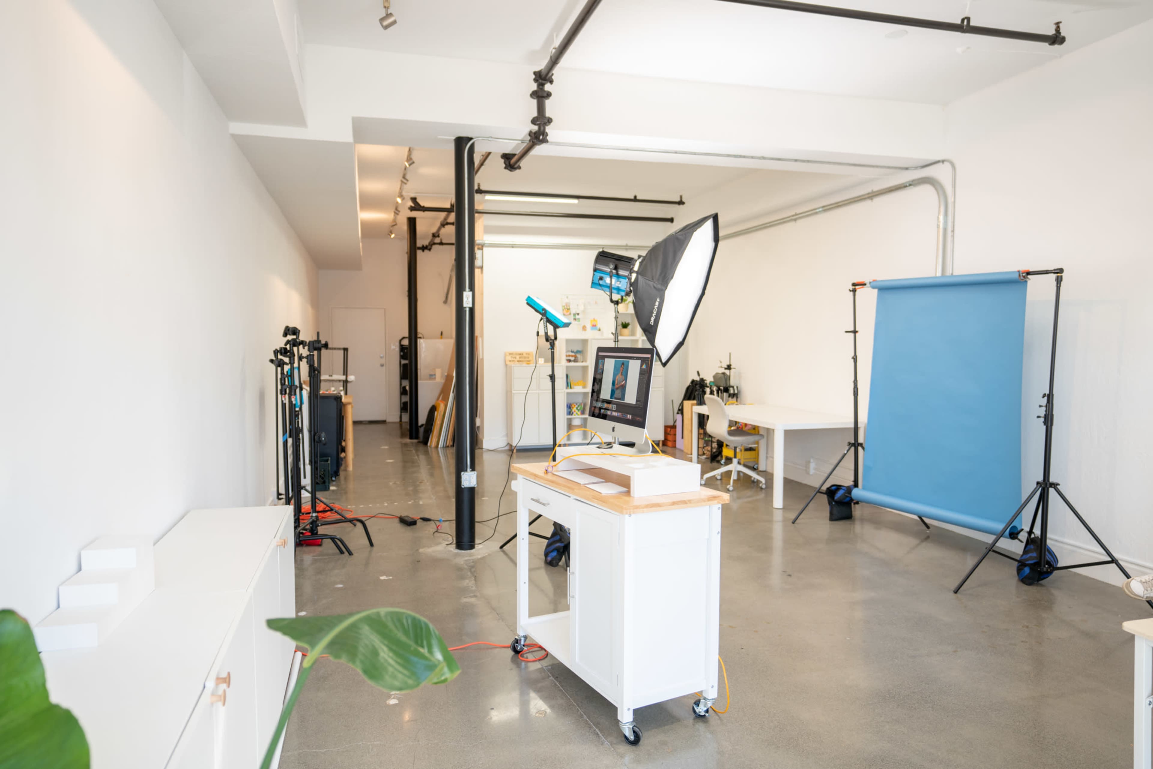 A spacious photography studio with a light setup, a computer on a work table, and a blue backdrop.