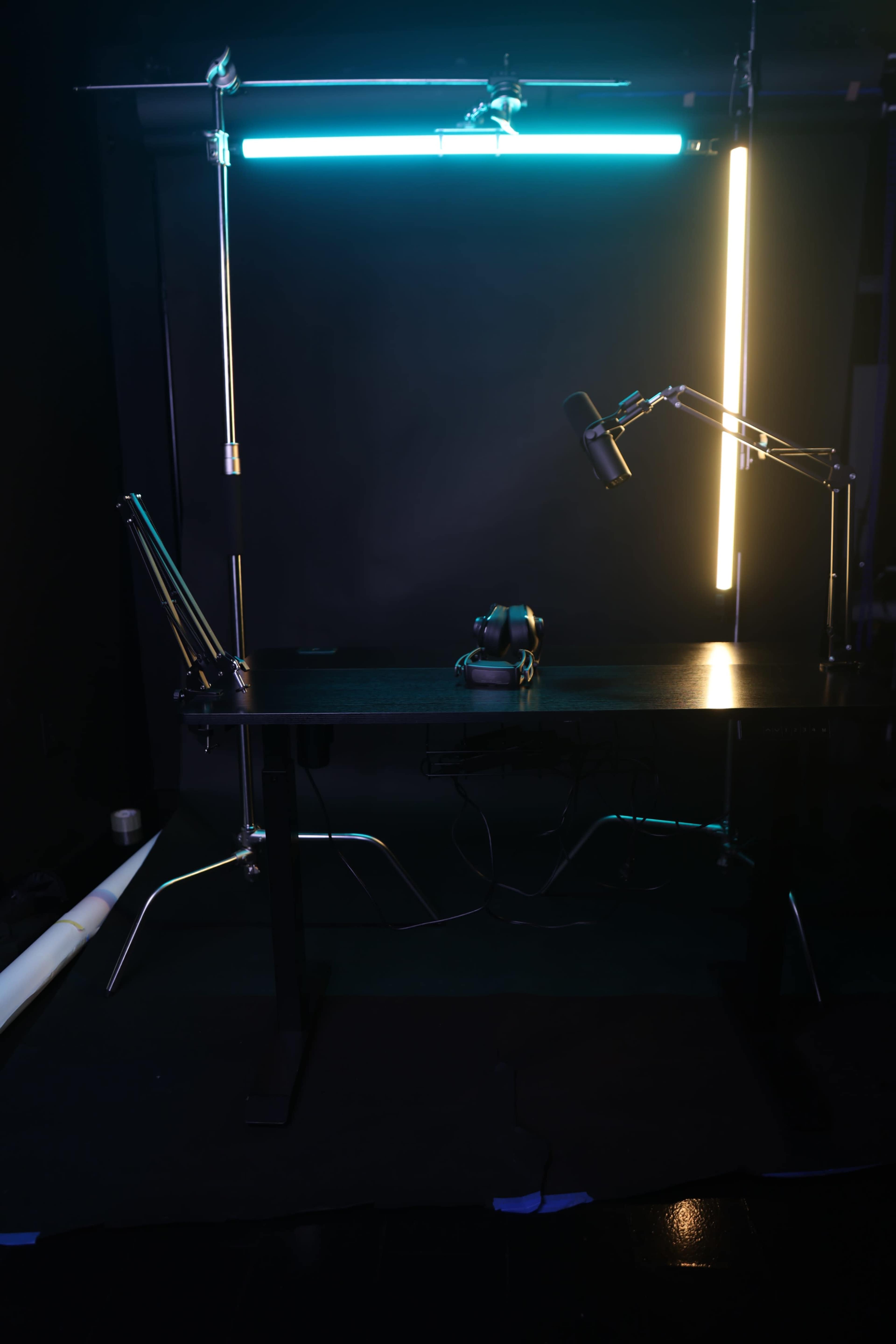 A dimly lit studio setup featuring a black table with a microphone attached to an arm, a camera on the table, and backdrop lights.