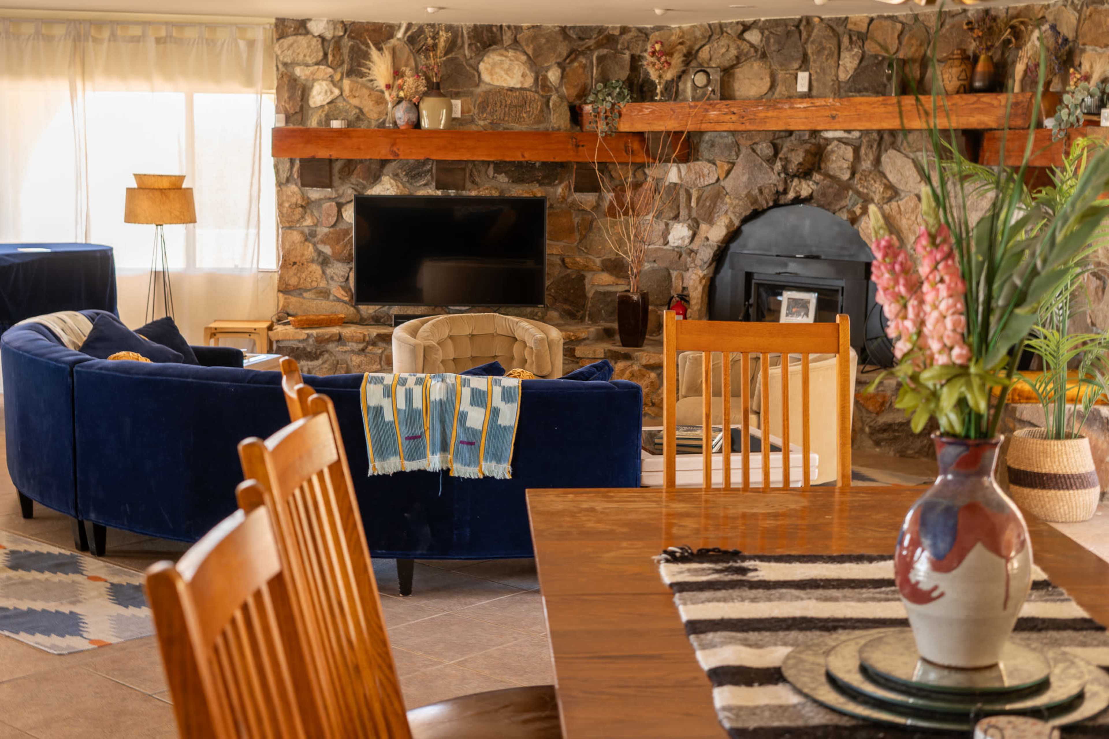 The image shows a cozy living area with a stone fireplace, a dark blue sofa, and a dining table in the foreground.