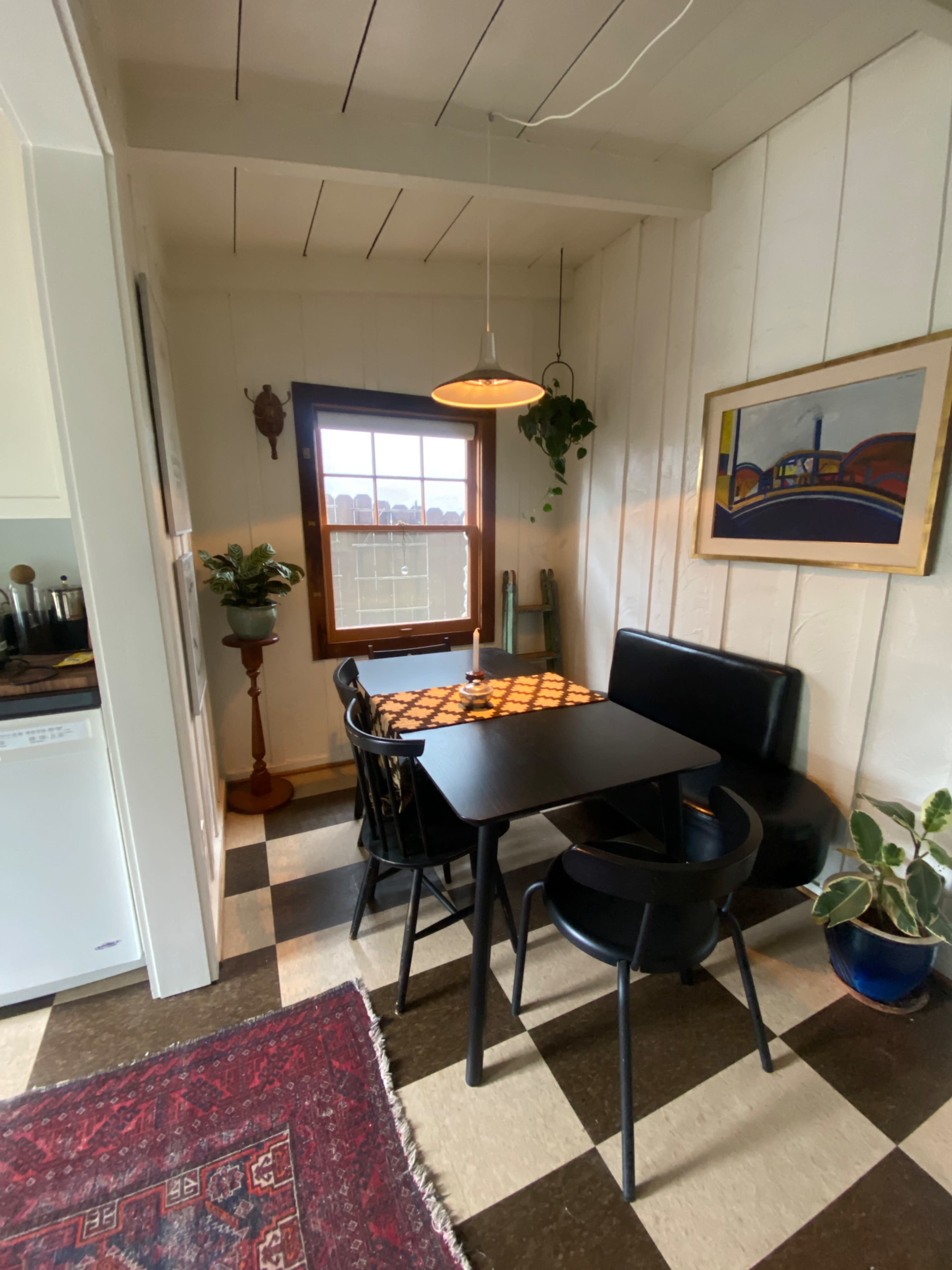 A small dining area features a black table with chairs, a window with a view, and a decorative rug on the floor.