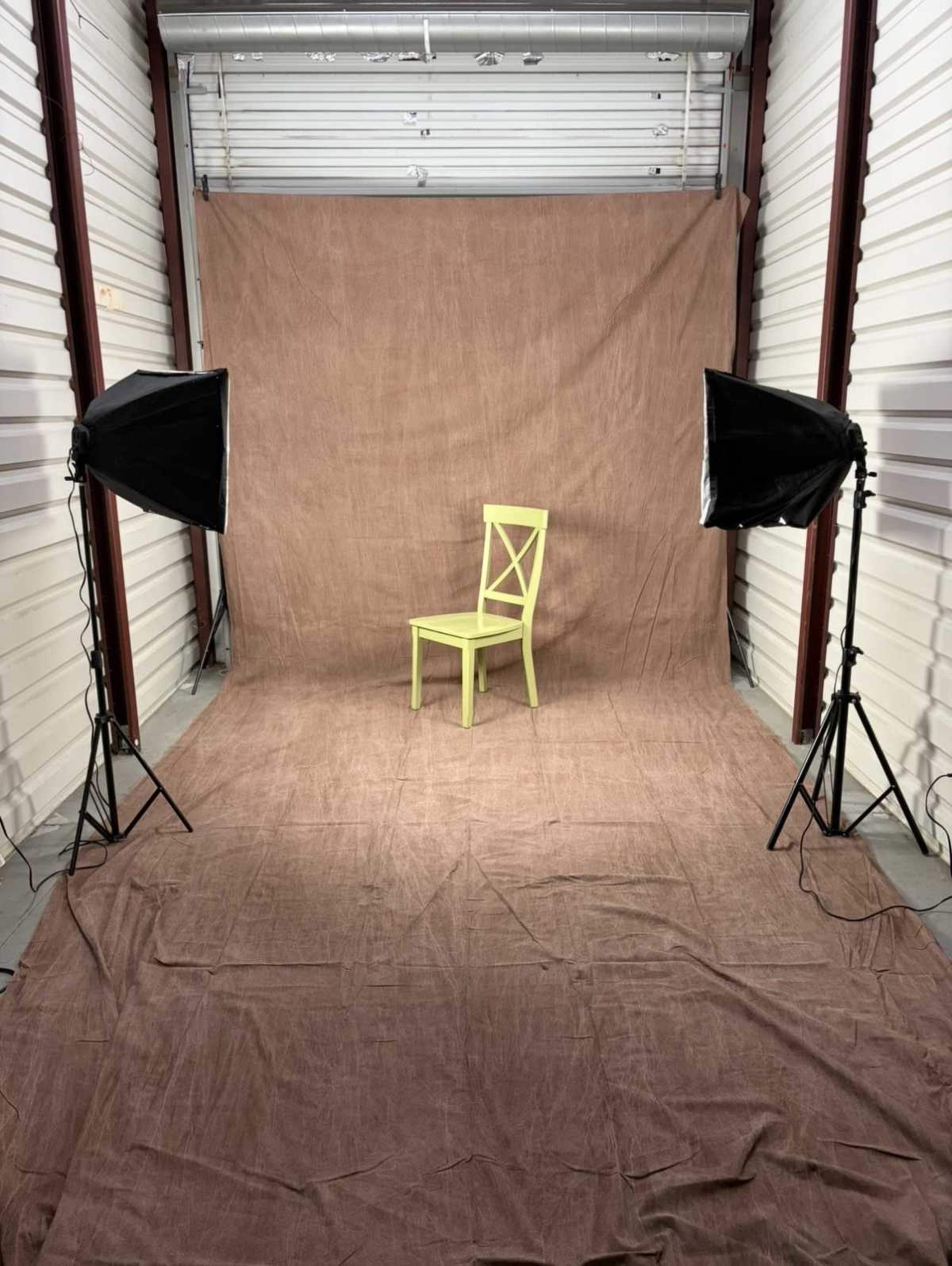 The image shows a bright green chair positioned in front of a brown backdrop, with two studio lights on either side.
