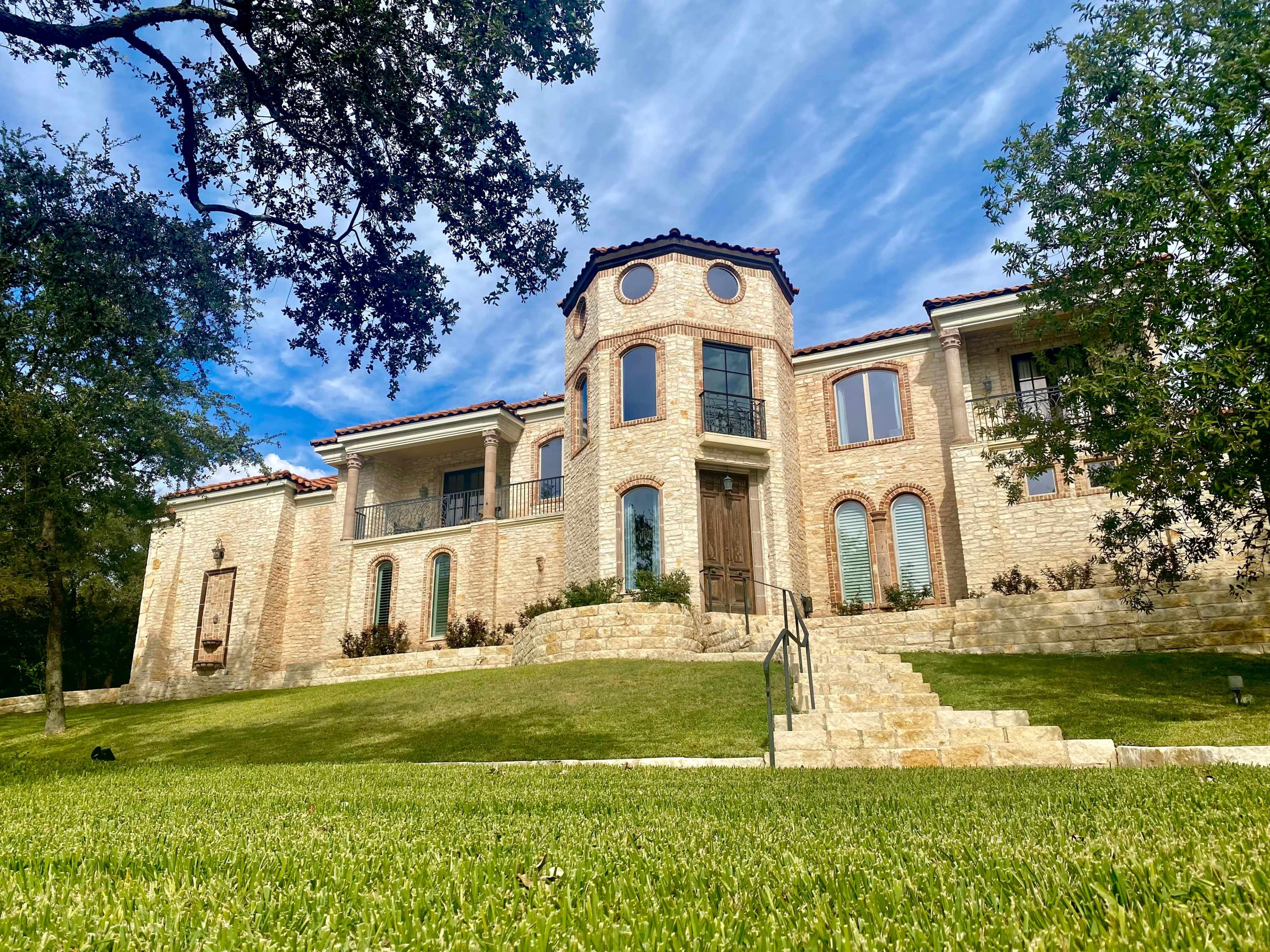 A large, two-story stone house with multiple circular windows is set on a grassy slope.