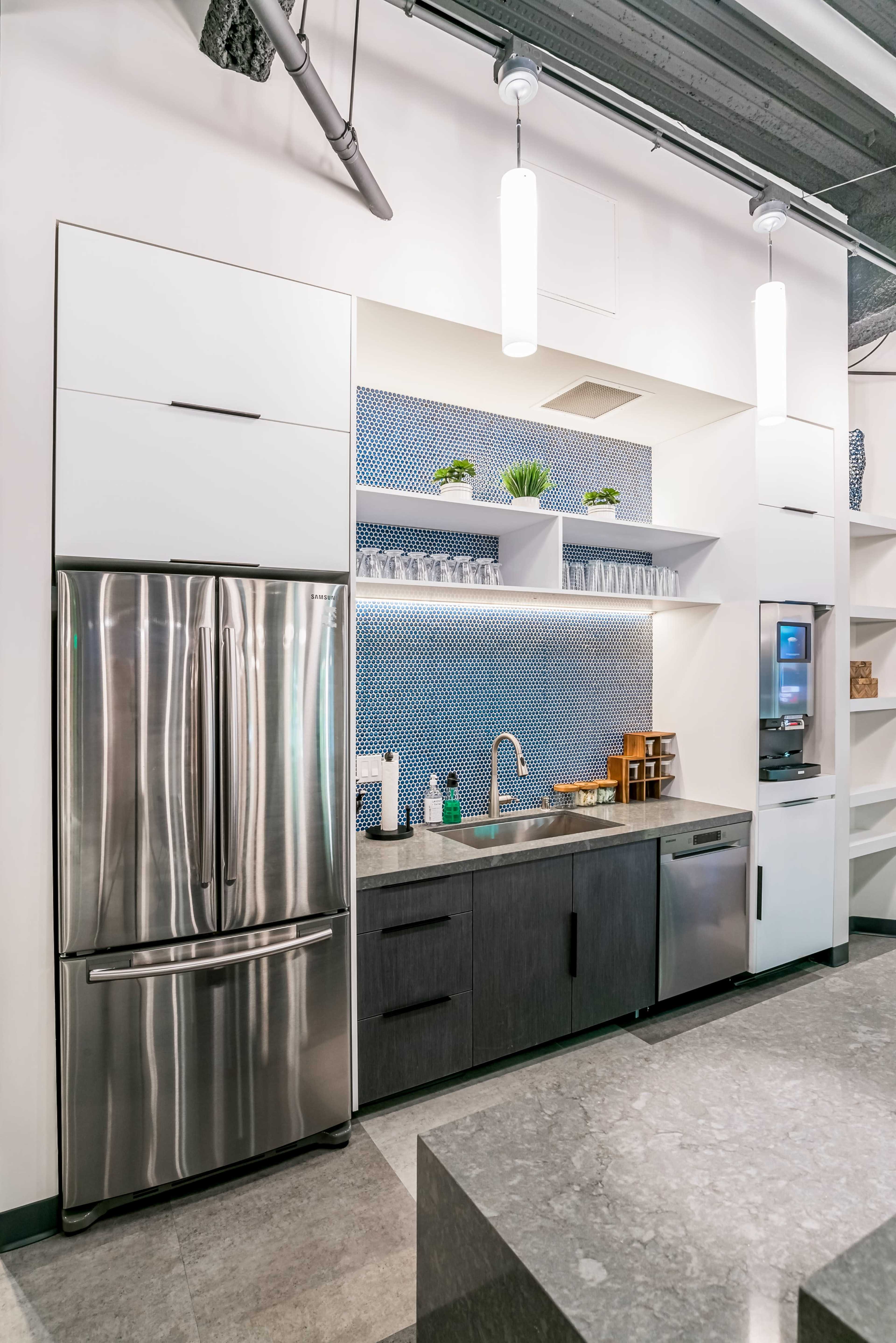 A modern kitchen with stainless steel appliances, including a refrigerator and sink, set against a blue patterned backsplash.