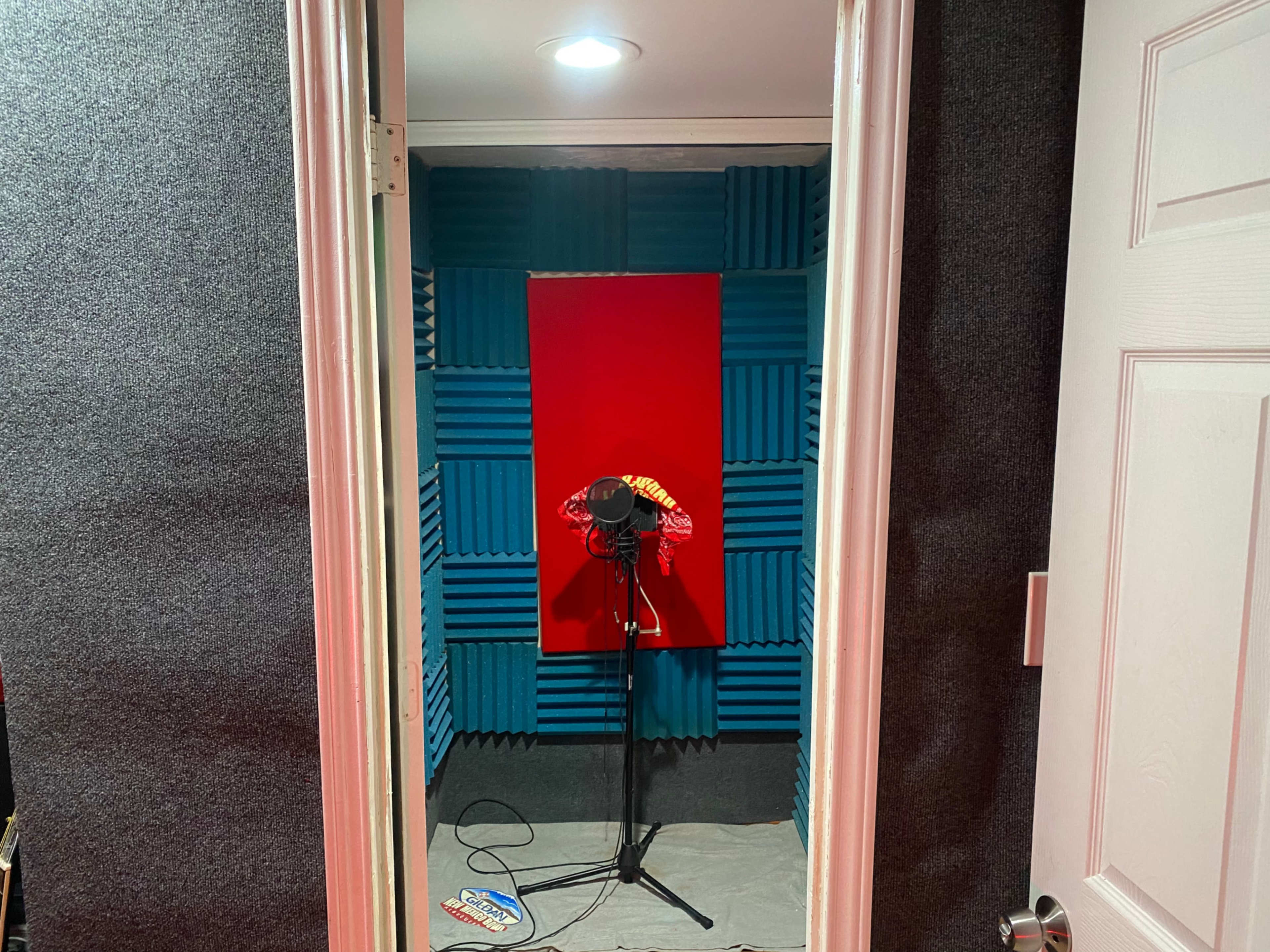 A small soundproof recording booth with blue and red acoustic foam panels, containing a microphone on a stand in the center.