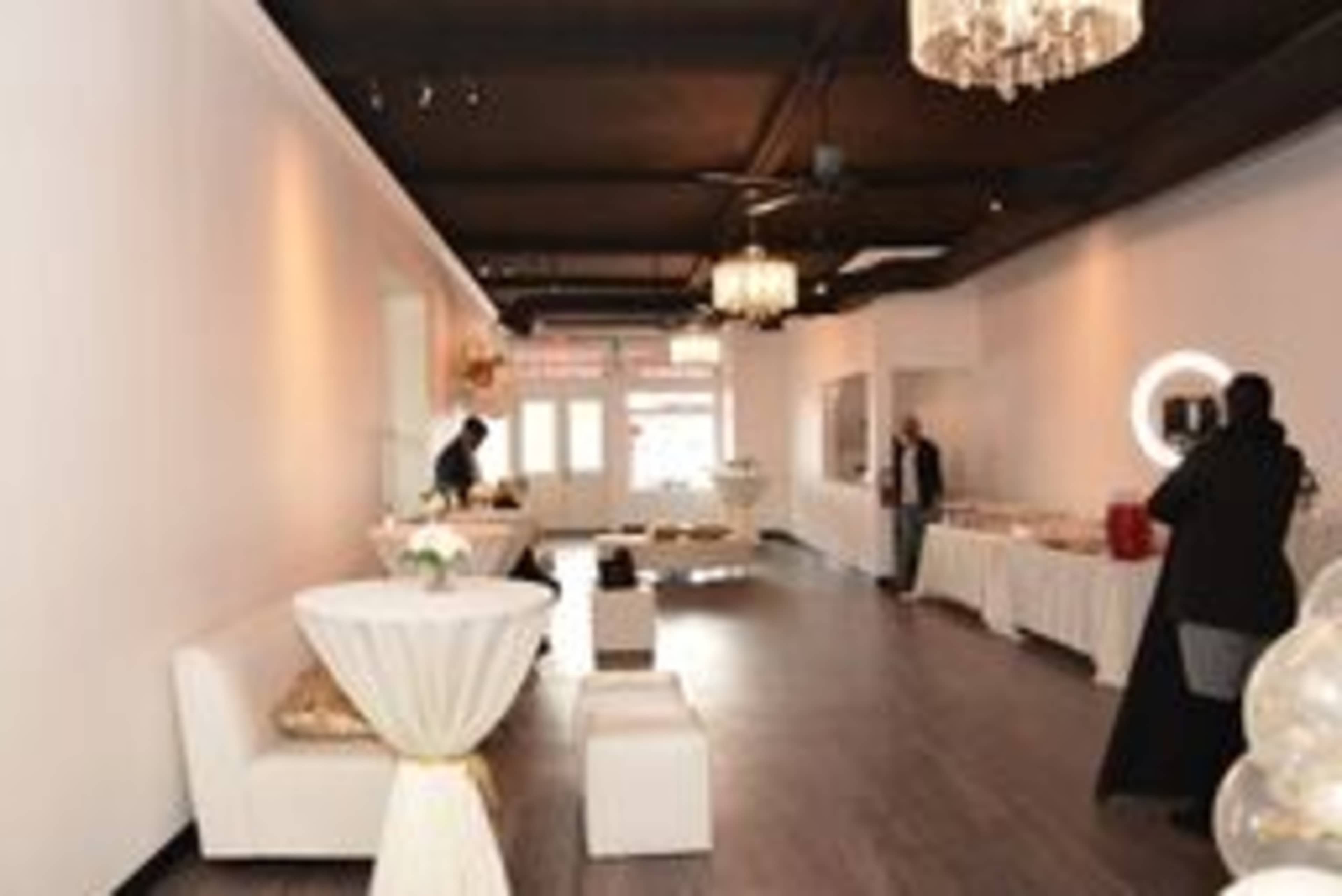 An elegantly decorated event space with white walls, dark wood floors, and tables set up for a gathering.