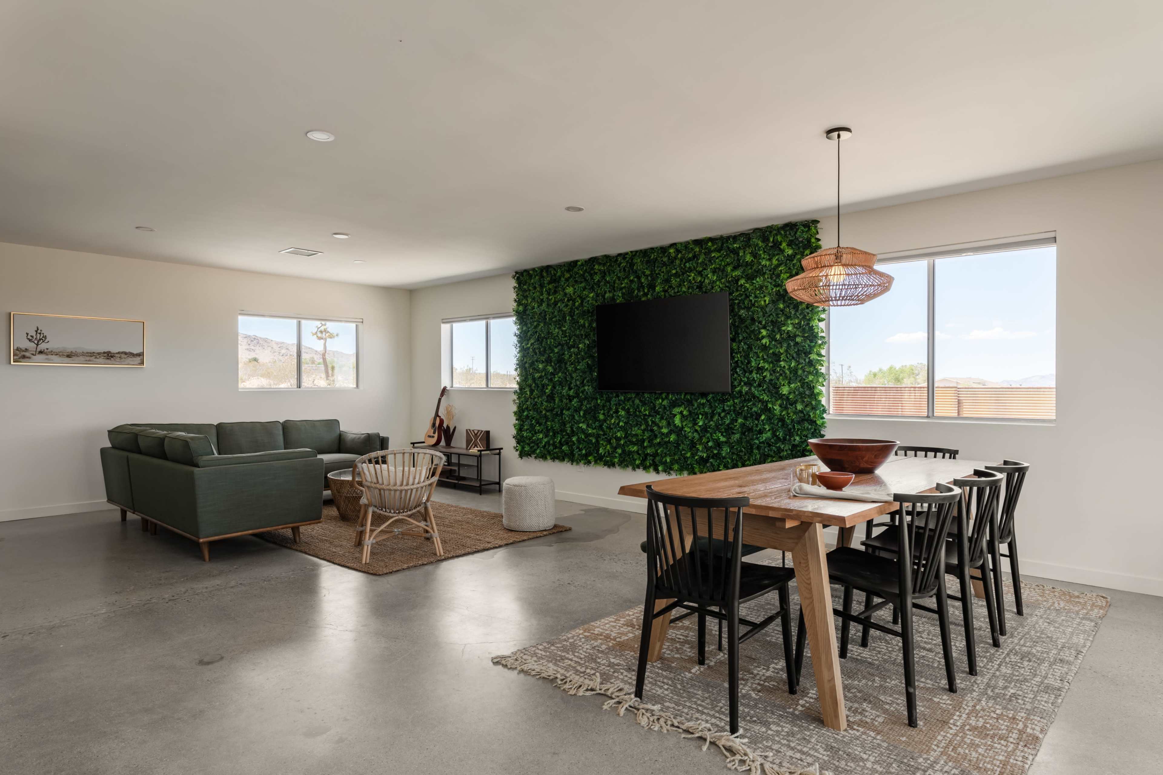 A modern living space features a green accent wall, sleek furniture, and a dining area with wooden table and black chairs.