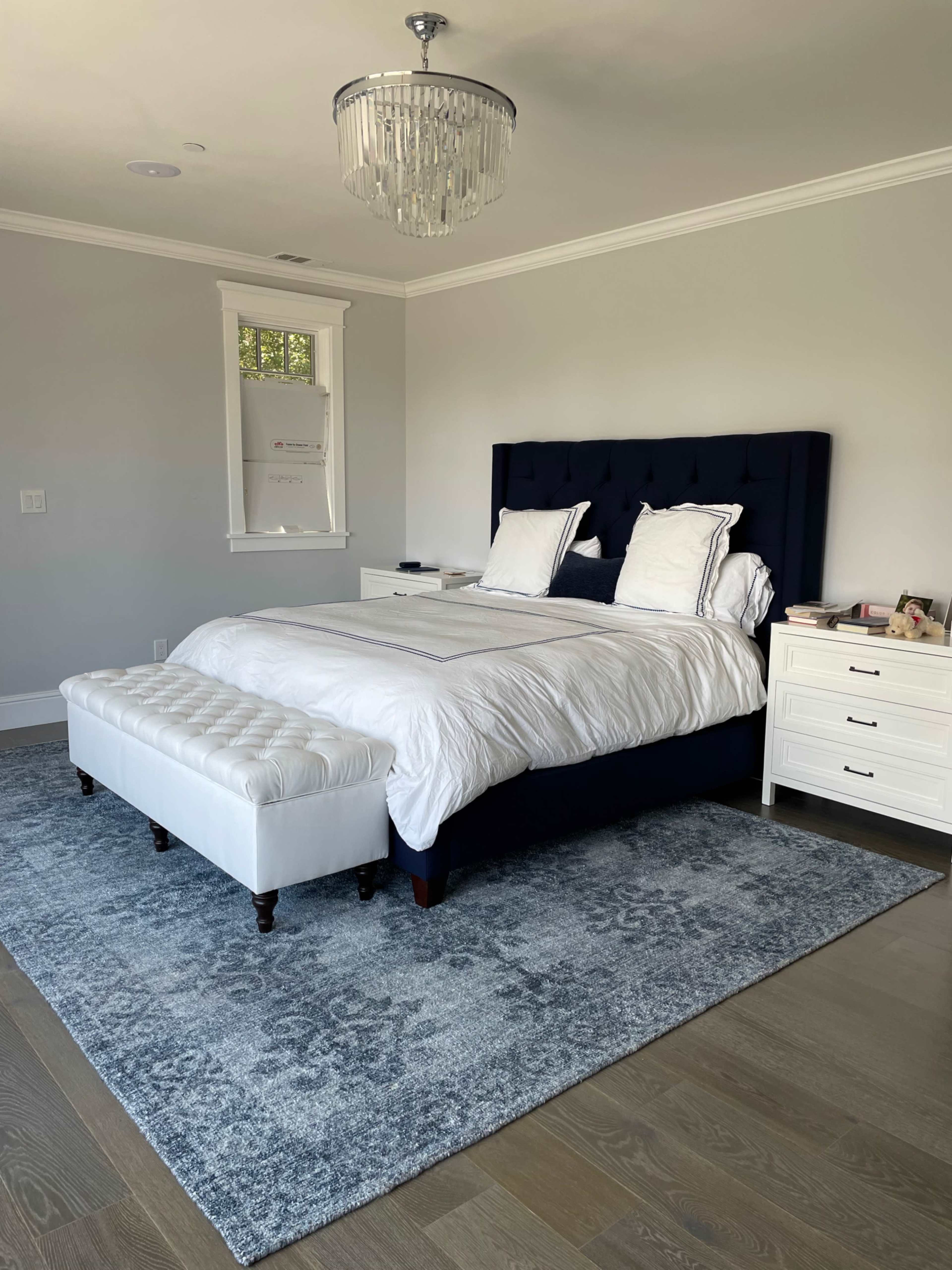 A stylish bedroom with a navy blue upholstered bed, white bedding, a light-colored rug, and a chandelier overhead.