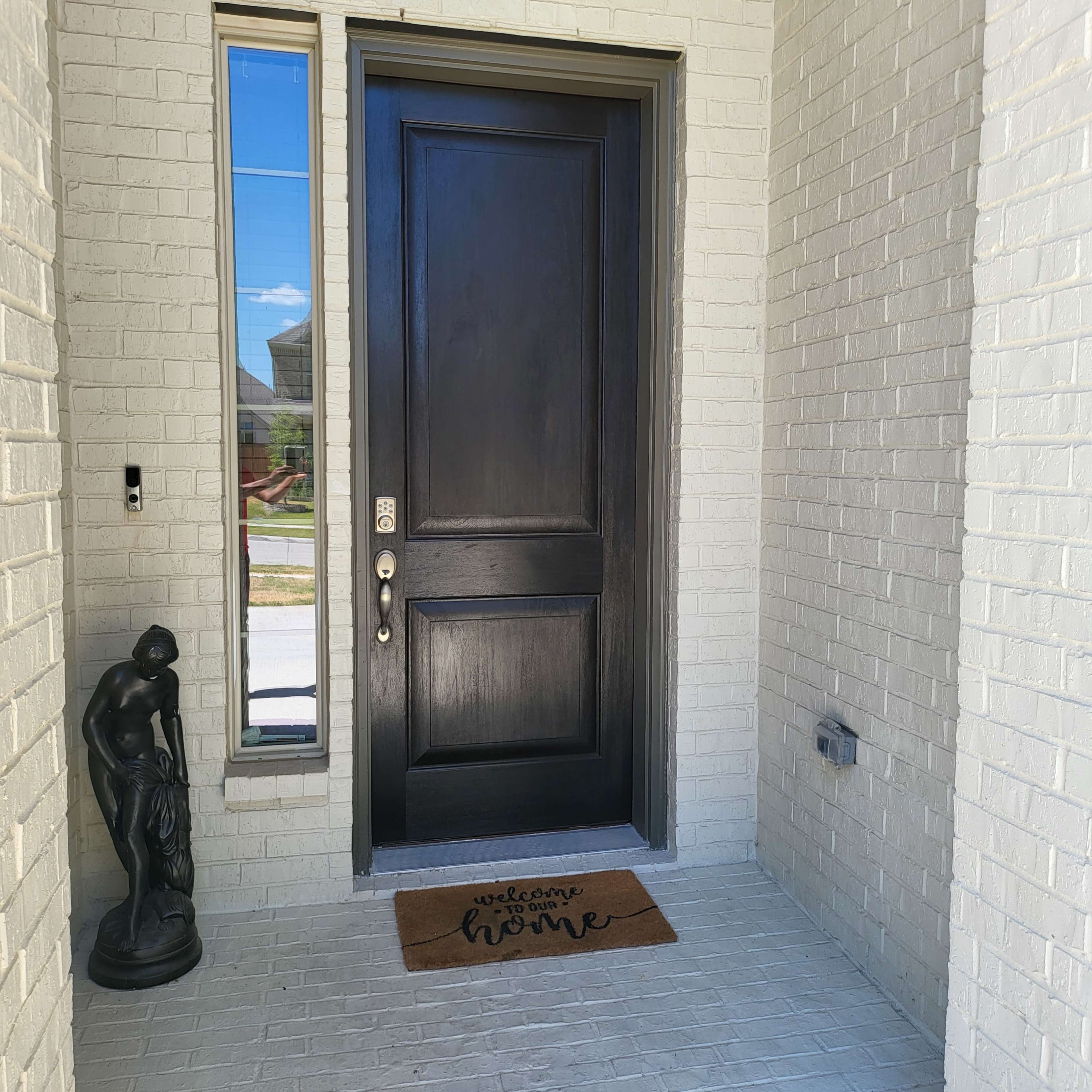 A front entrance with a black door, a welcome mat reading "welcome home," and a decorative statue next to the door.