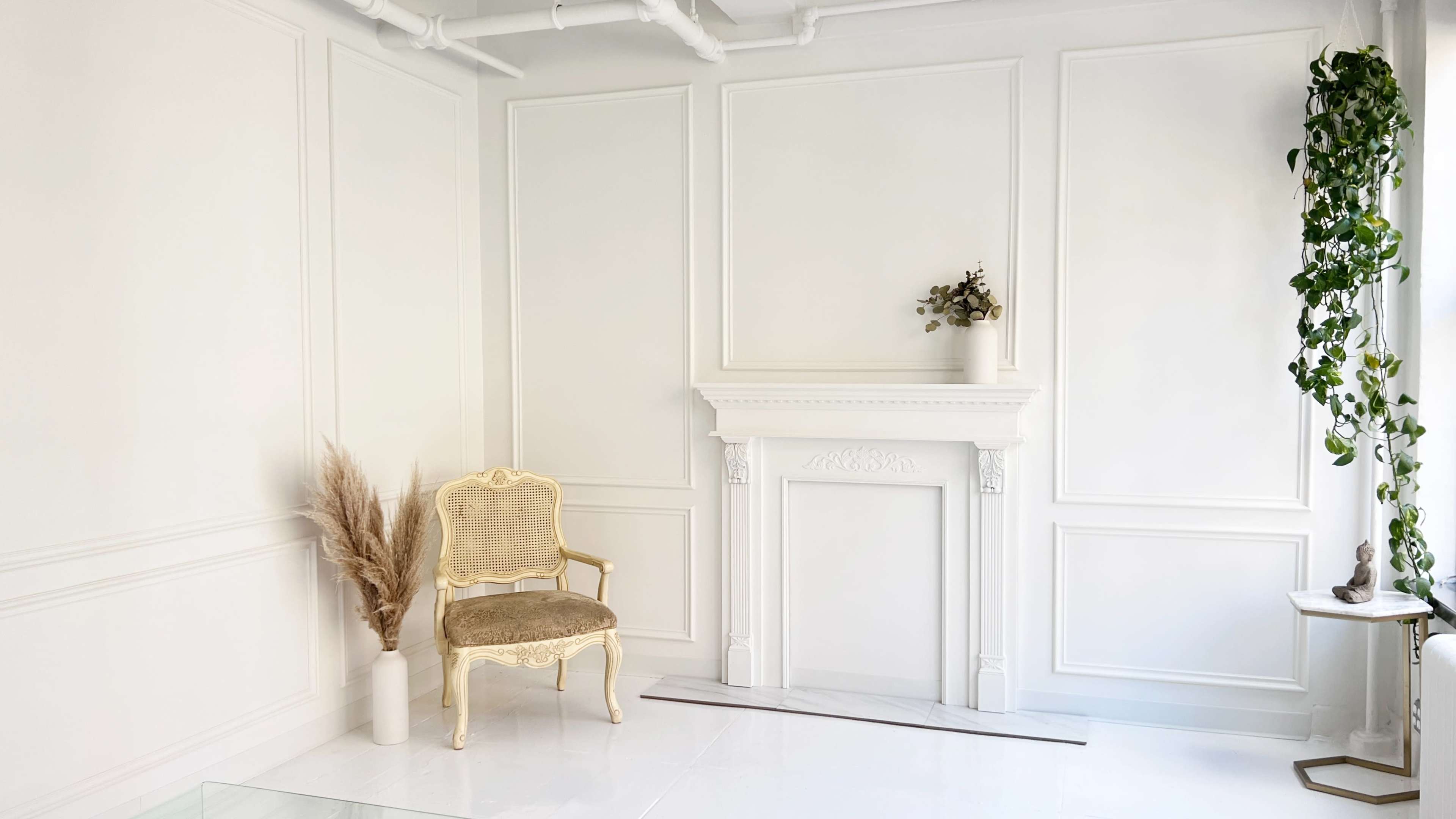 A minimalist room with white walls, a decorative fireplace, a gold chair, and potted plants.