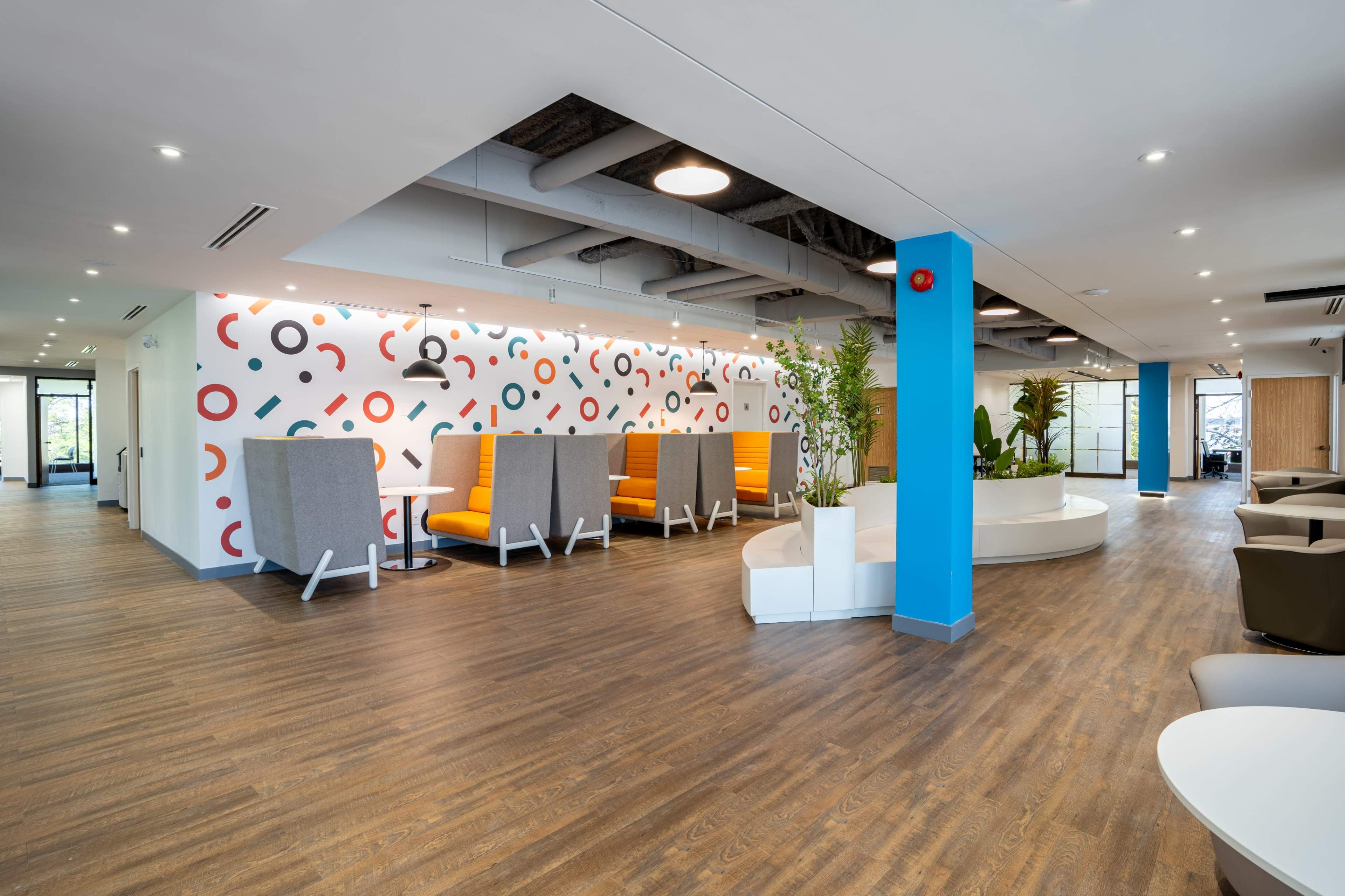 A modern office space featuring a mix of seating areas, colorful wall decor, and wood laminate flooring.