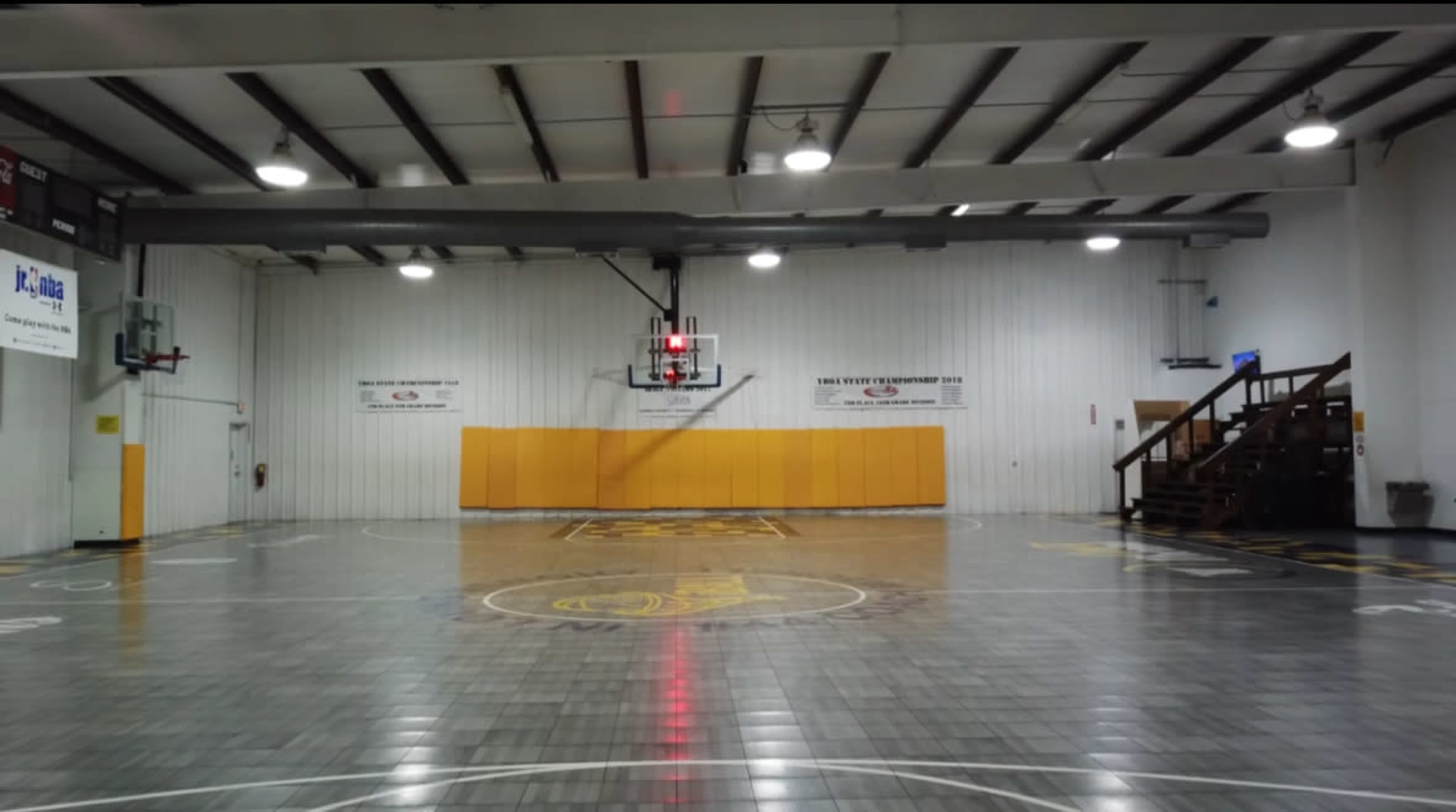 The image shows an empty indoor basketball court with two basketball hoops at either end and a wooden bleacher in the background.