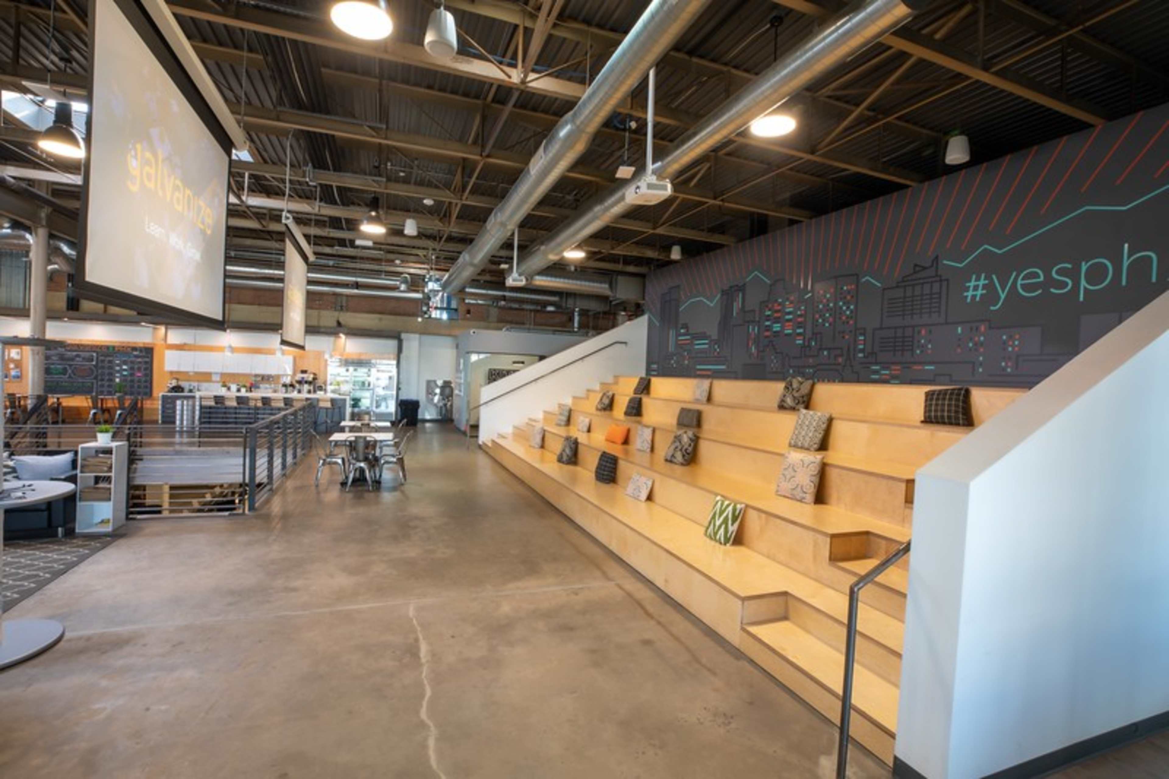 The image shows a modern interior space with wooden stair-like seating, a large screen displaying "yesph," and colorful wall graphics.