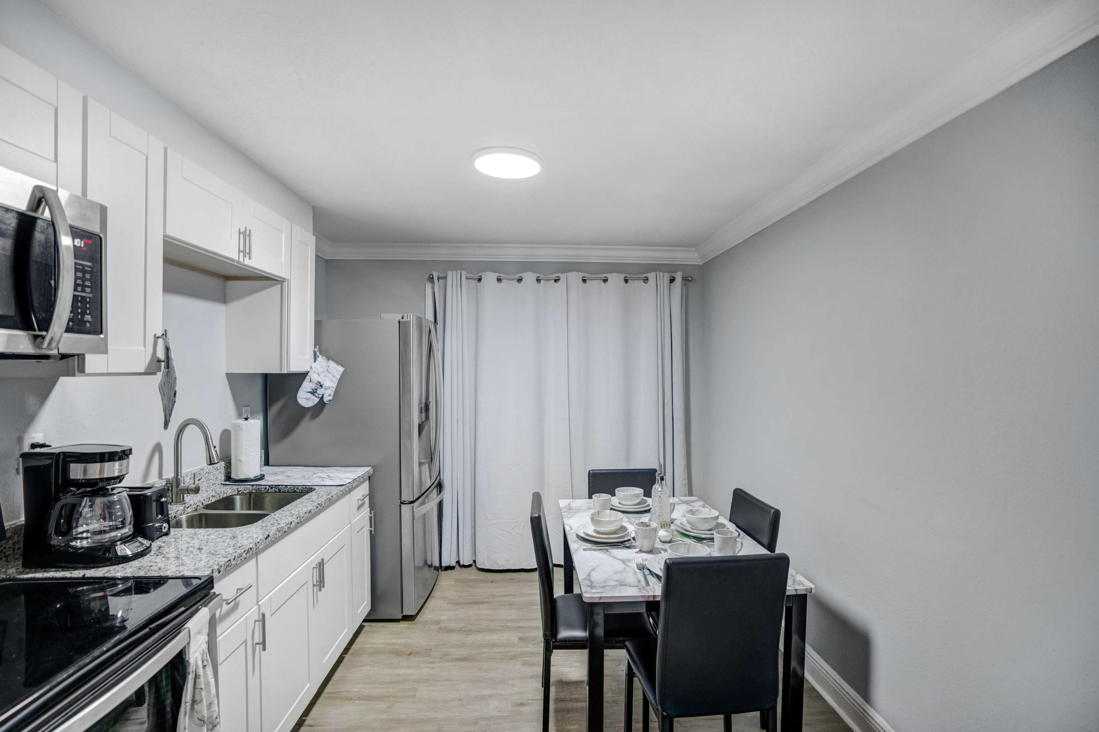 A modern kitchen featuring stainless steel appliances, white cabinetry, and a small dining table set for four.