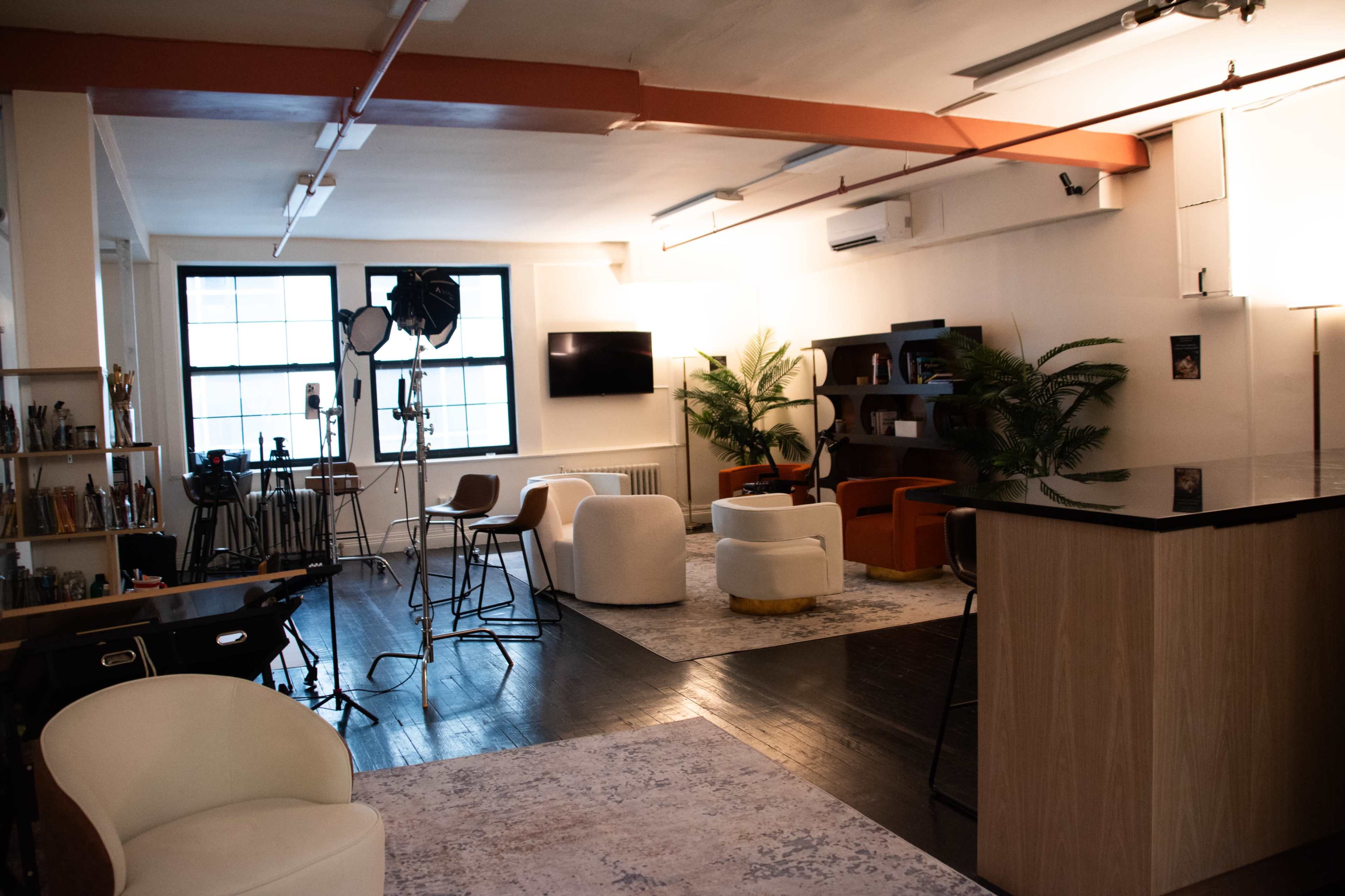 The image shows a spacious, modern studio with a seating area, a bar counter, and equipment setup for filming.