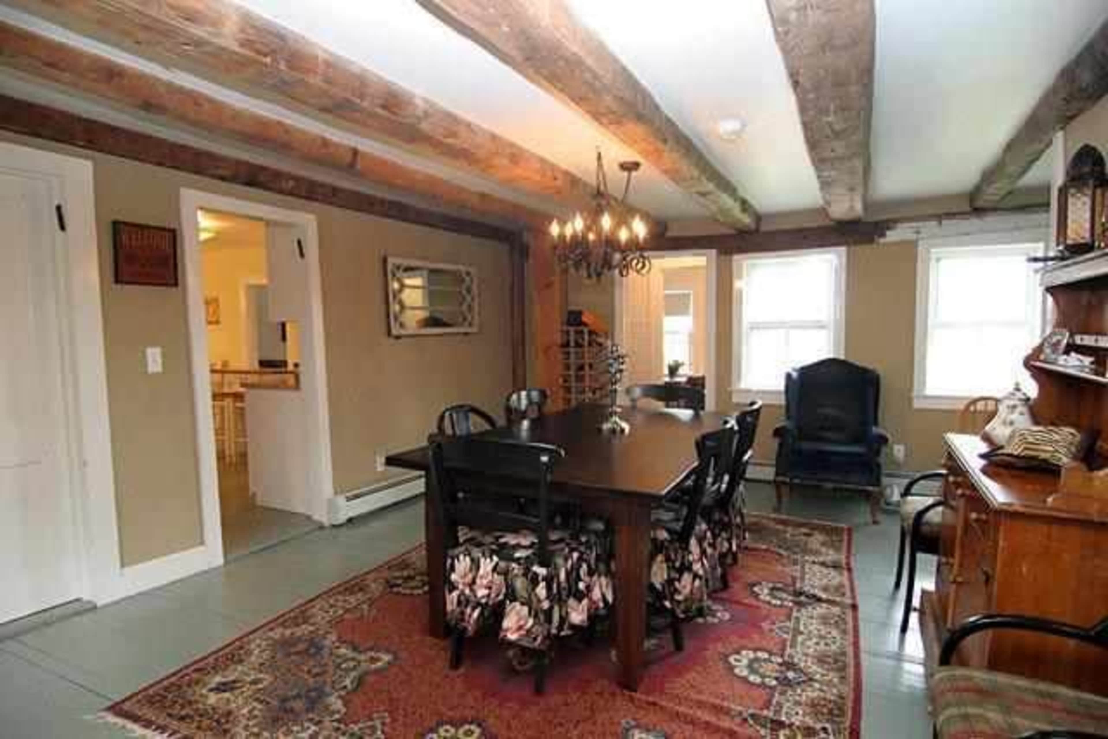 A rustic dining room with a large wooden table surrounded by black chairs, a chandelier overhead, and exposed wooden beams on the ceiling.
