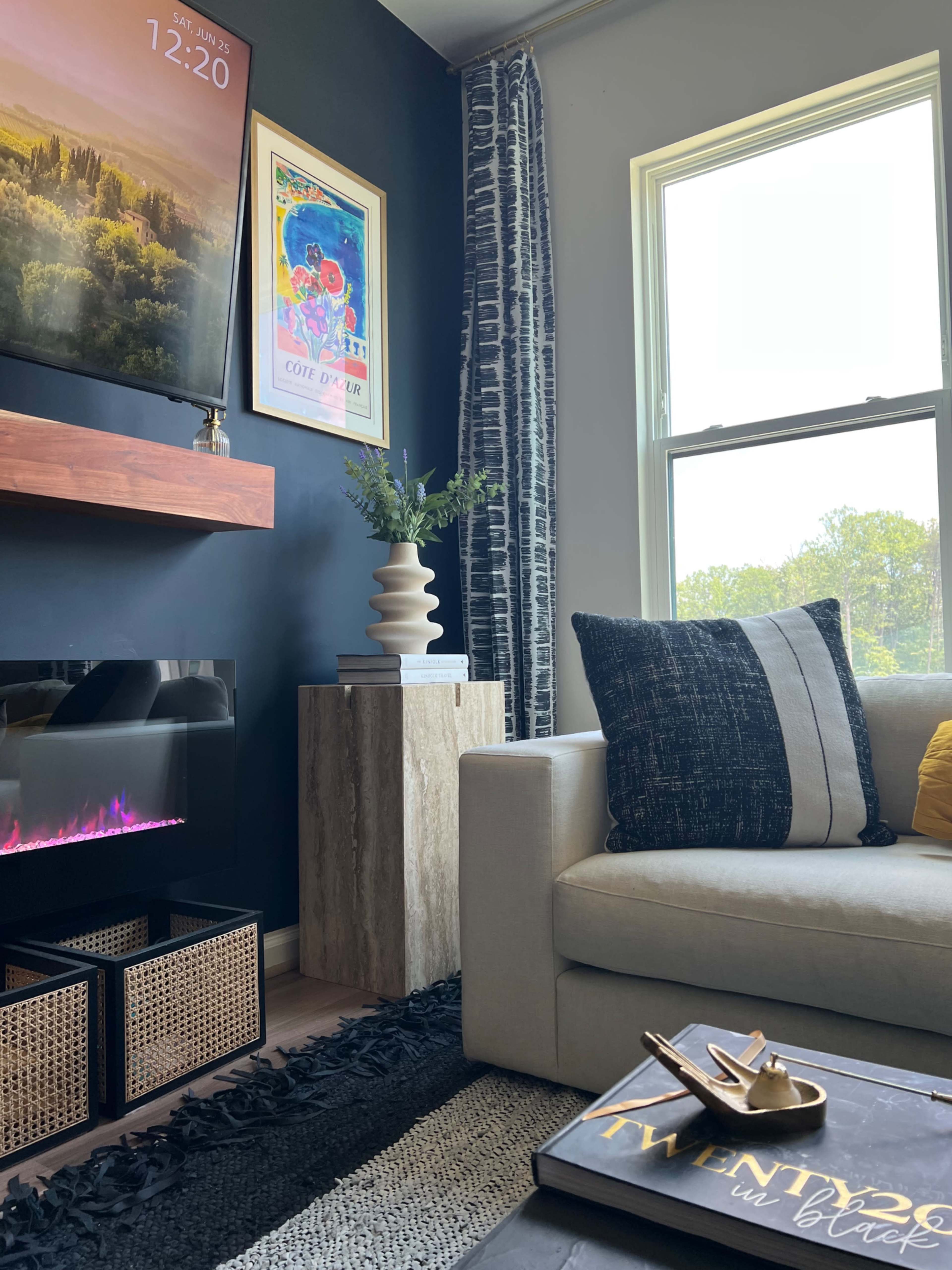 A modern living room featuring a light-colored sofa with decorative pillows, a wall-mounted television, a stylish plant vase, and a faux fireplace with a cozy ambiance.