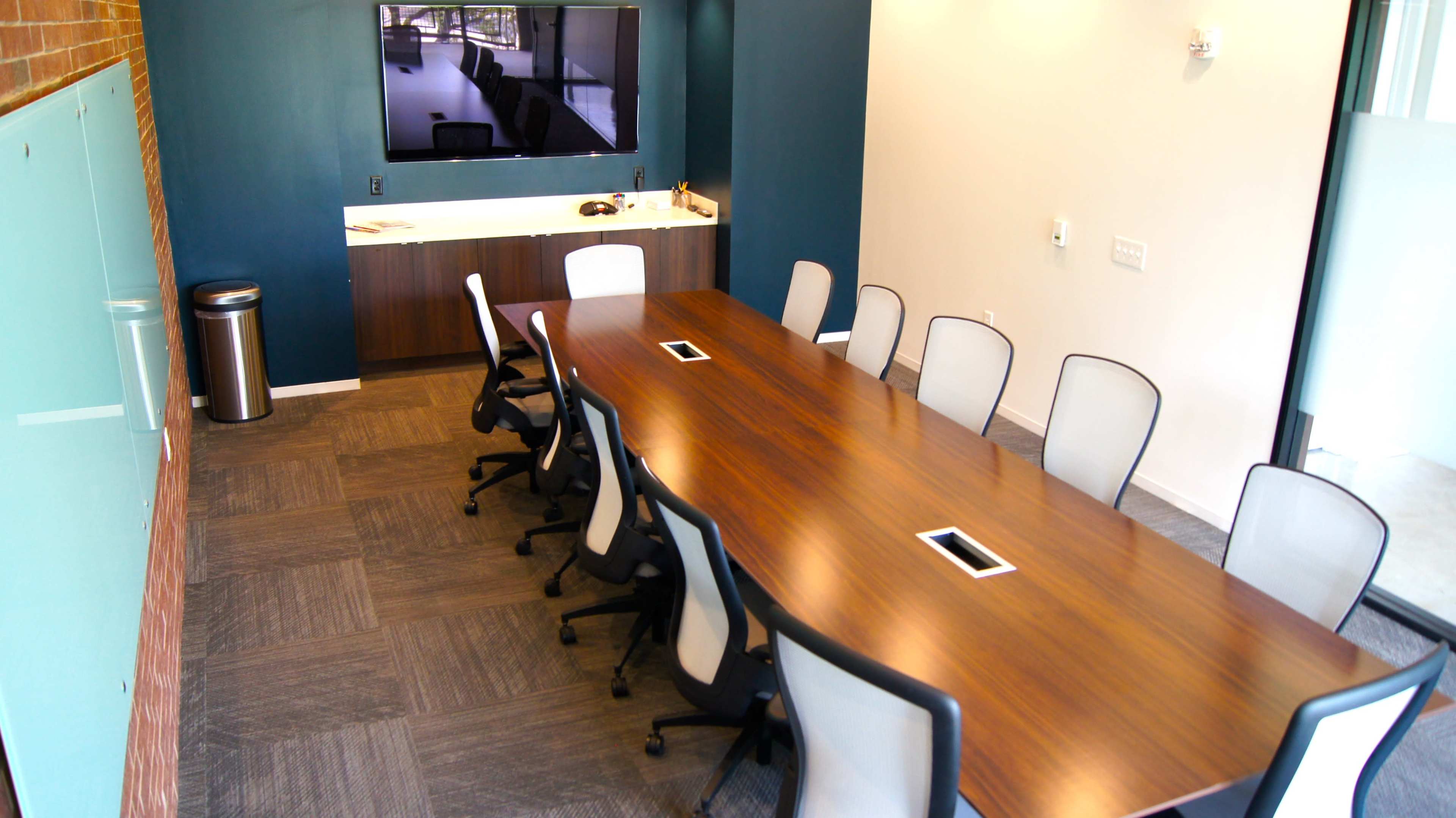 A modern conference room with a long wooden table and several ergonomic chairs arranged around it.