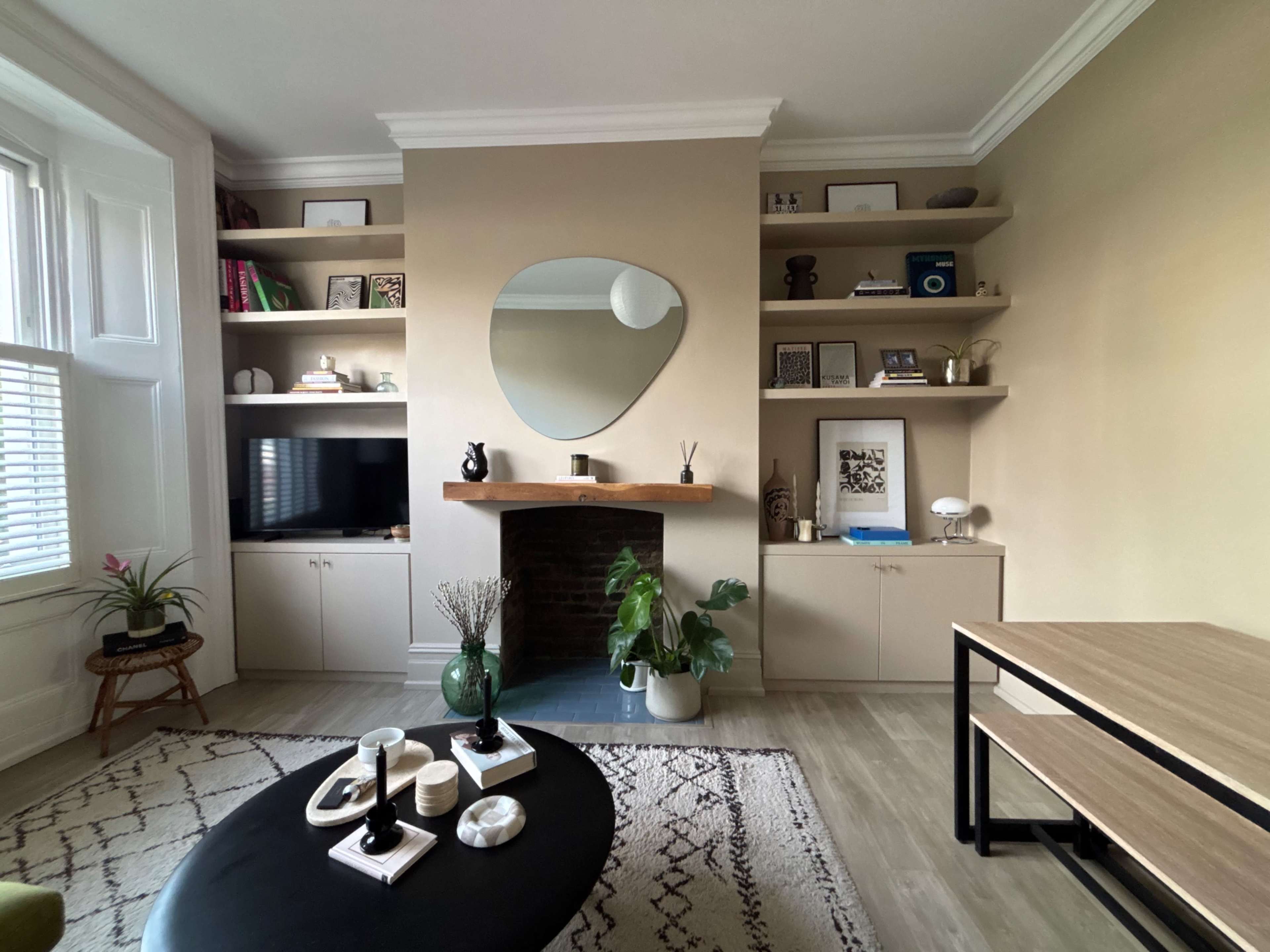 The image shows a modern living room with a fireplace, built-in shelves, and a coffee table, featuring minimalist decor and potted plants.