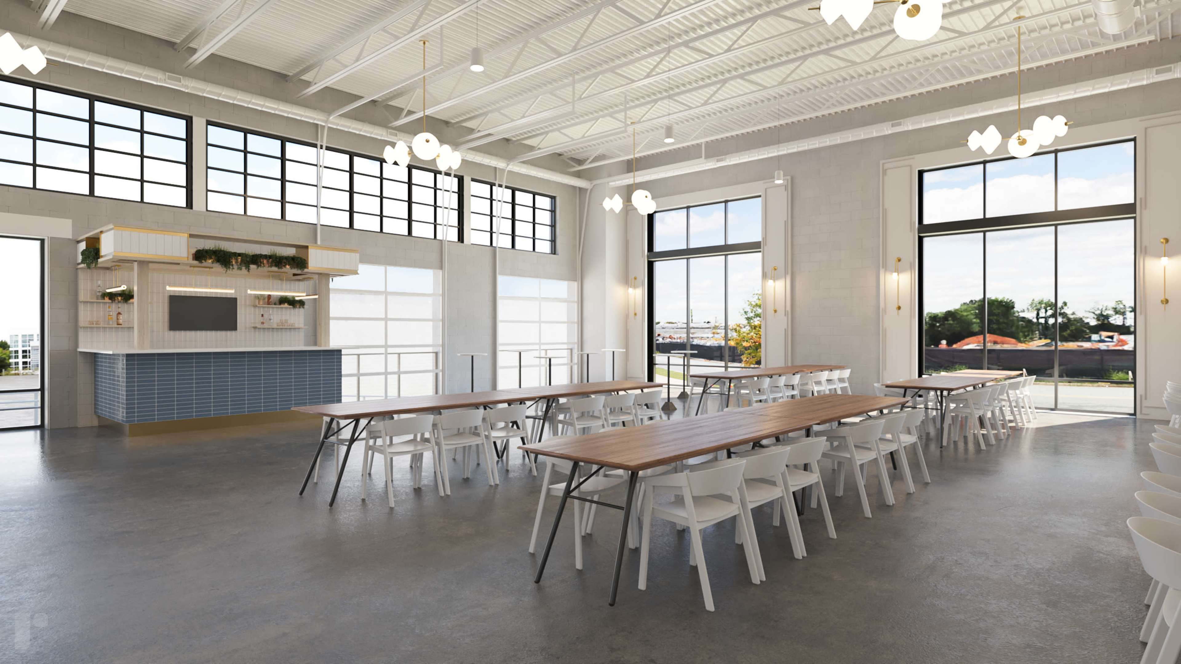 The image shows a spacious event hall with long wooden tables and white chairs, large windows allowing natural light, and a setup area with a decorative wall.