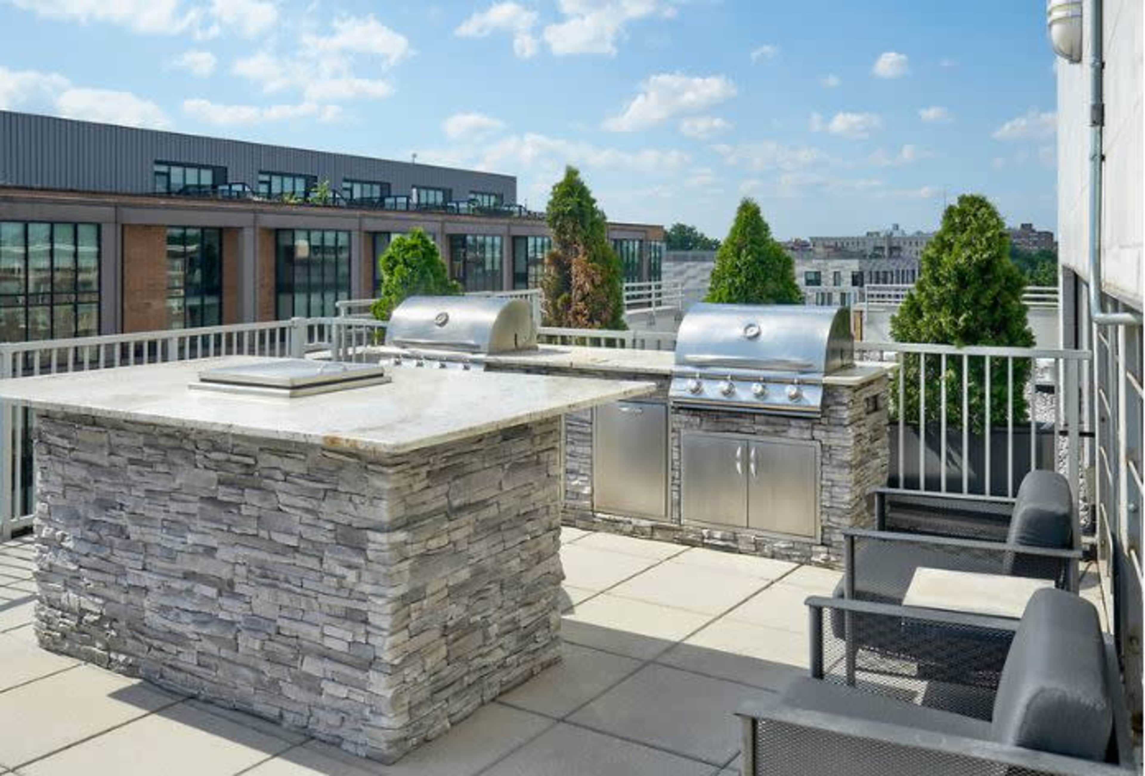 A rooftop terrace features a stone outdoor kitchen with two stainless steel grills and seating.