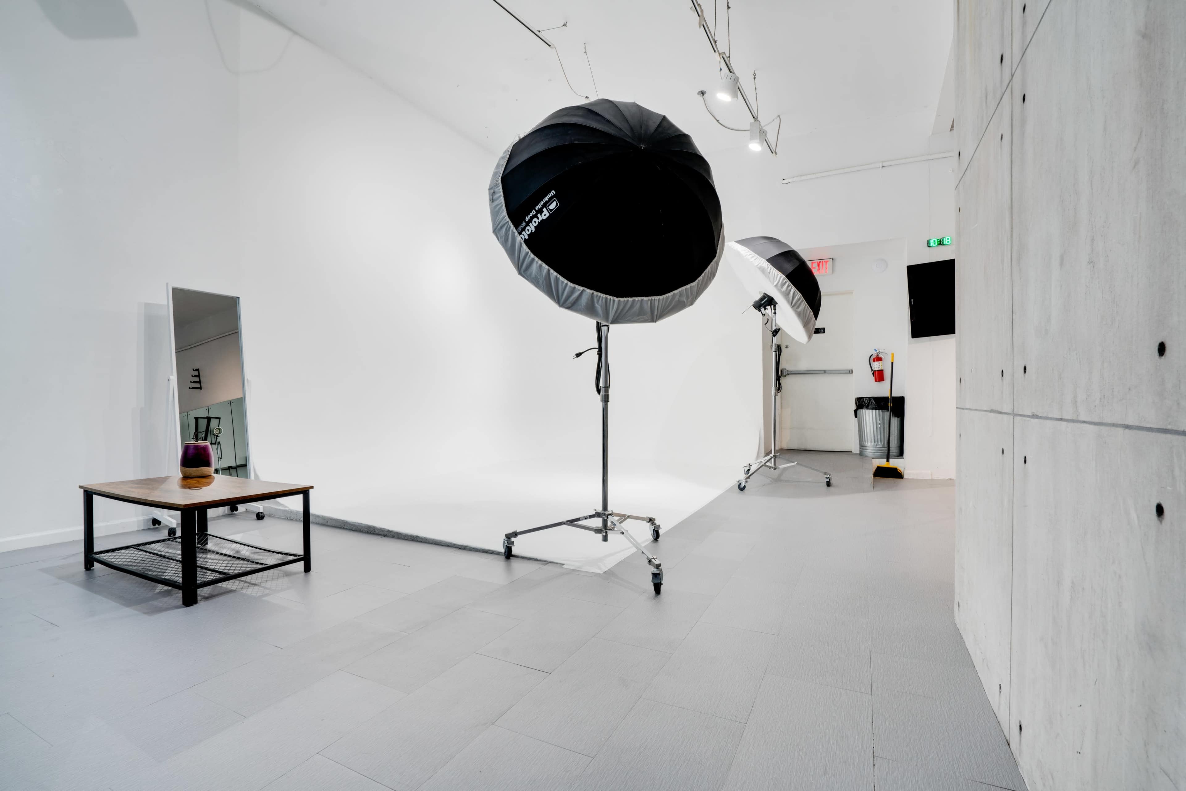 A photography studio with large softbox lights, a mirror, and a minimalistic setup featuring a gray floor and white backdrop.