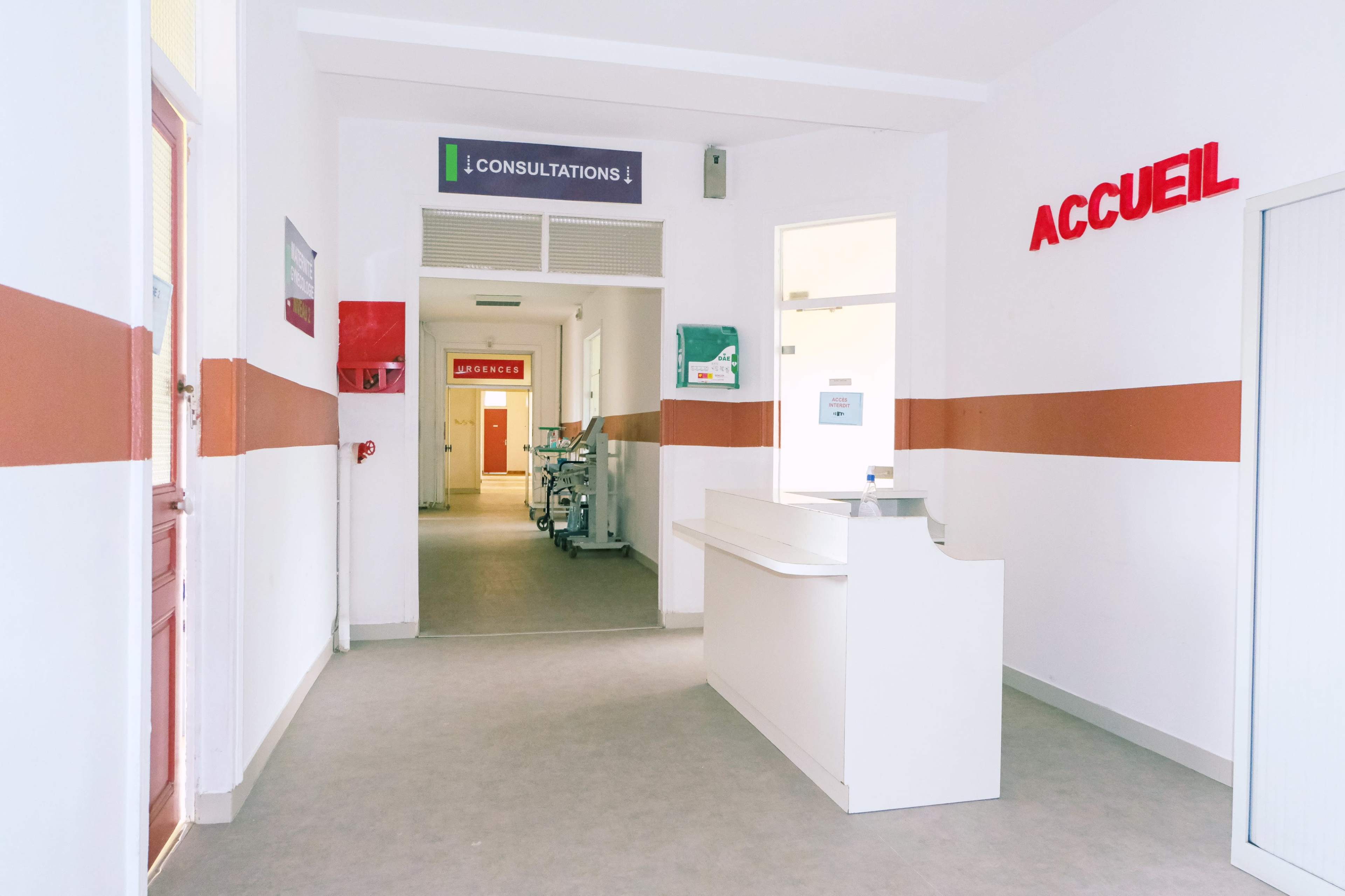 A well-lit corridor in a healthcare facility with a reception desk and signs indicating consultations and welcome areas.