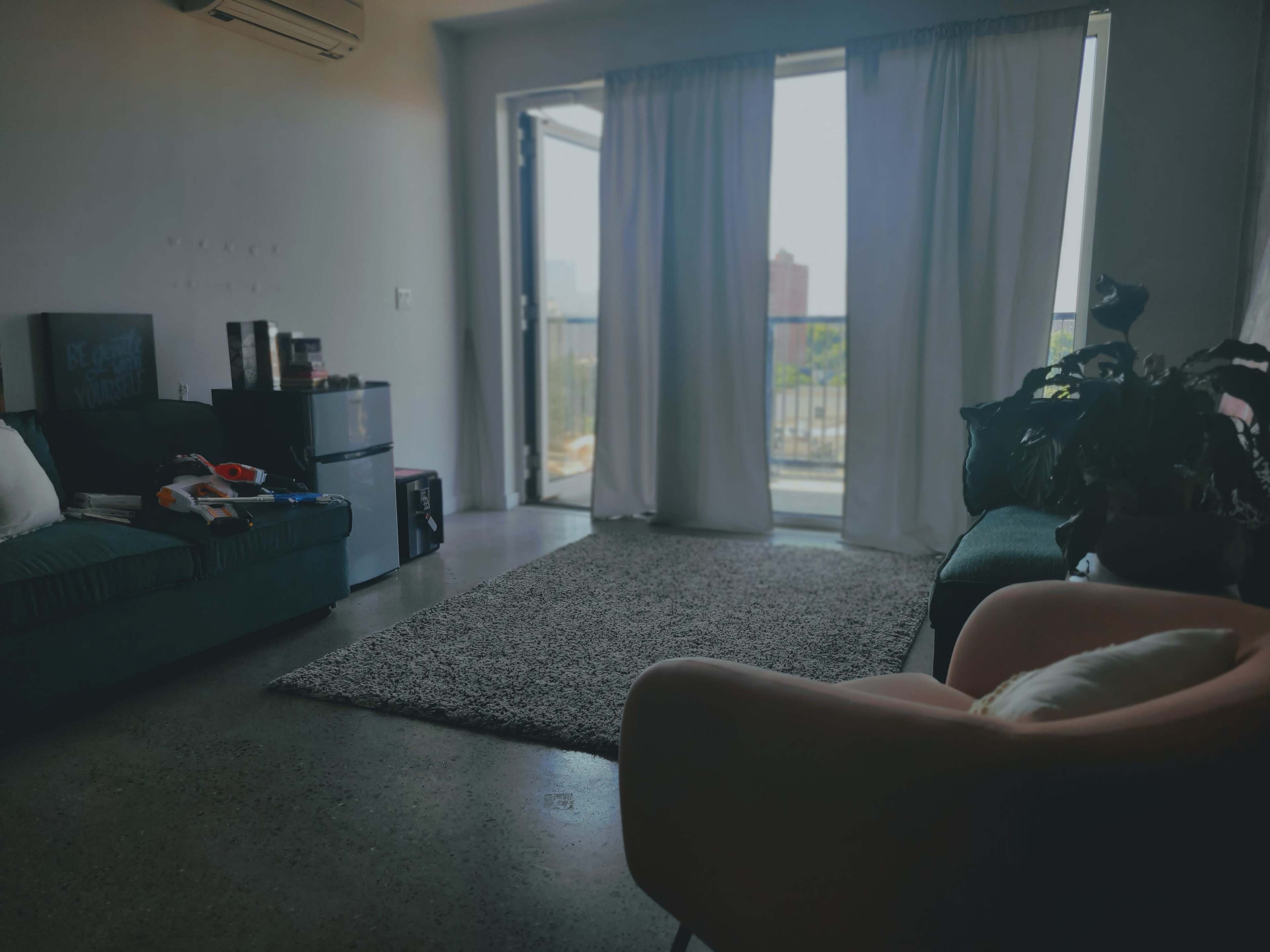 A living room features a sofa, a chair, and a large window with sheer curtains overlooking a balcony.