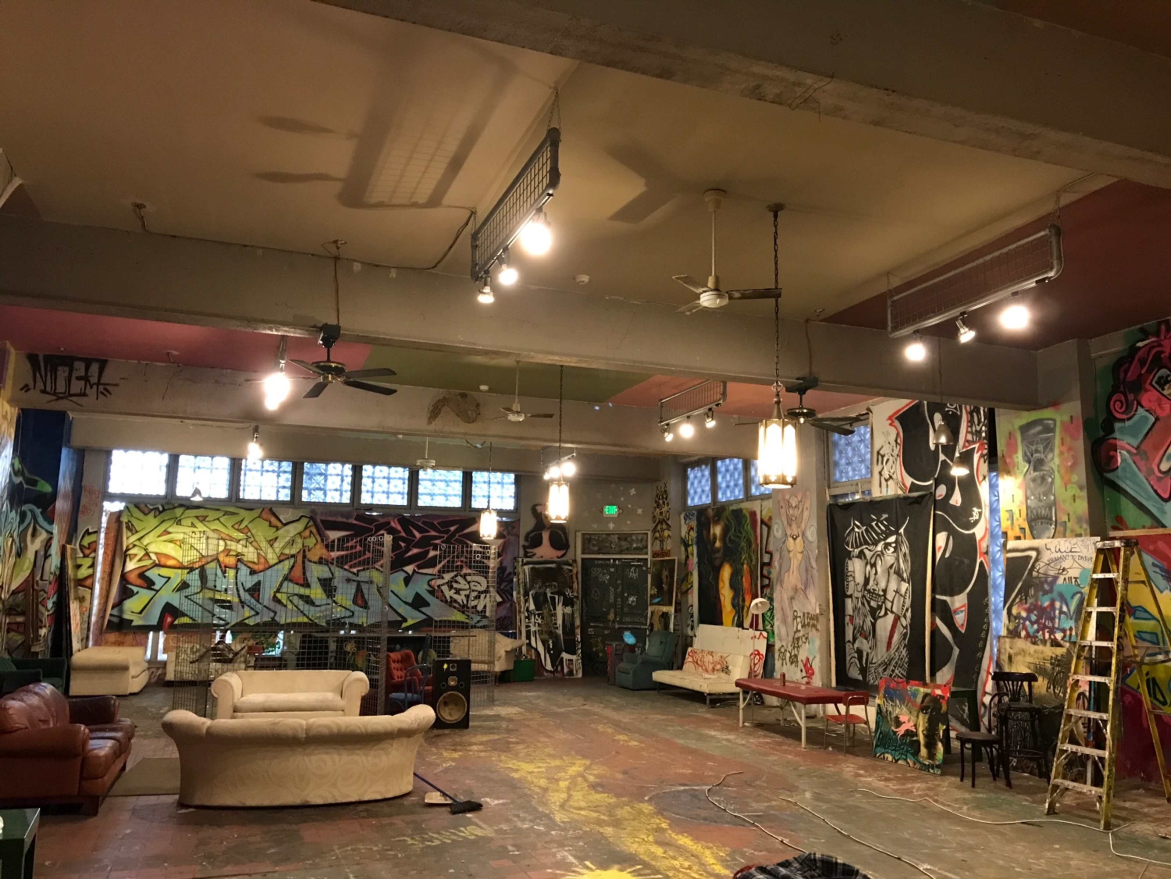 A spacious room filled with colorful graffiti on the walls, featuring a mix of seating arrangements, lights, and art supplies scattered throughout.