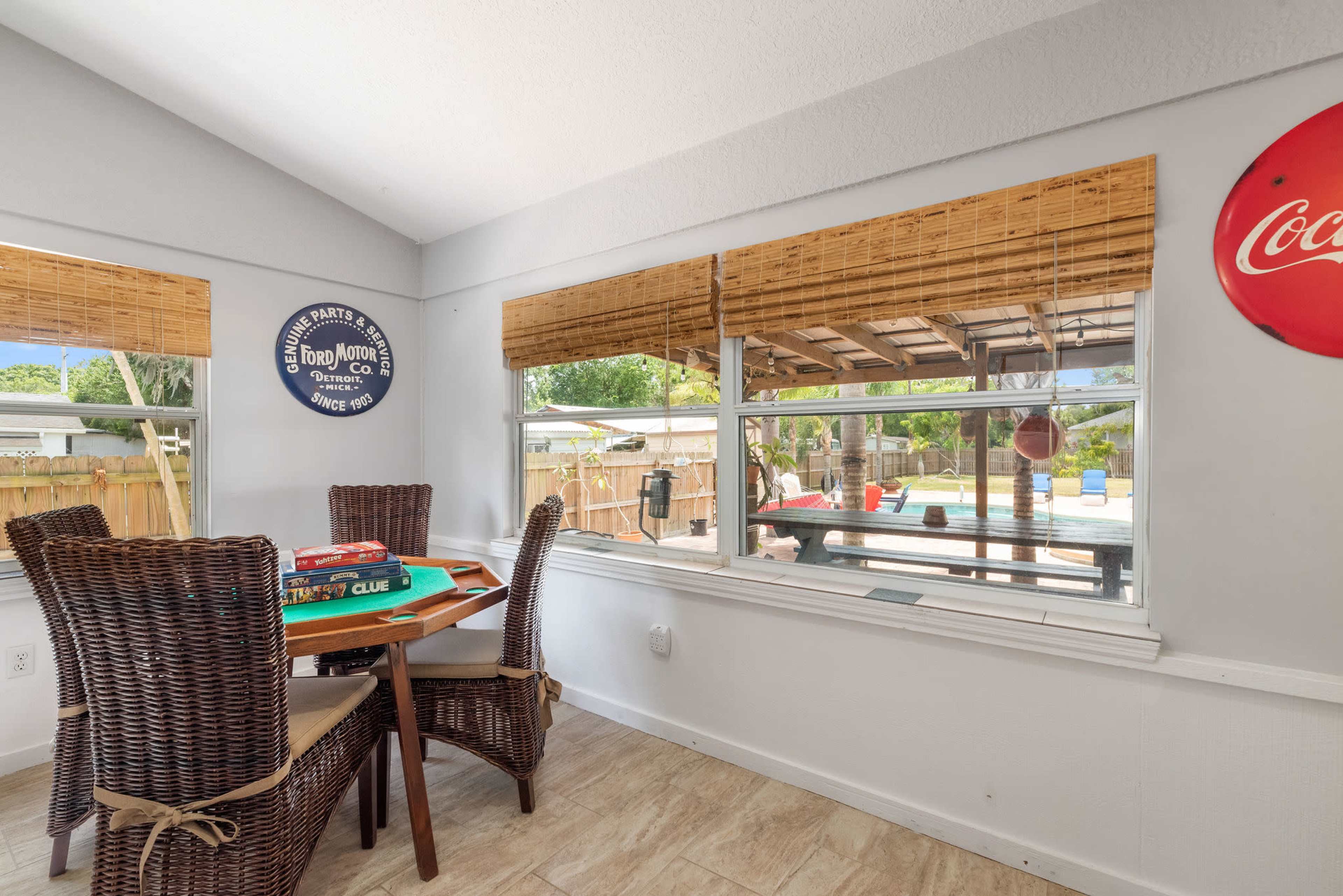 A cozy dining area with a table and chairs overlooks a covered outdoor space and a swimming pool through large windows.