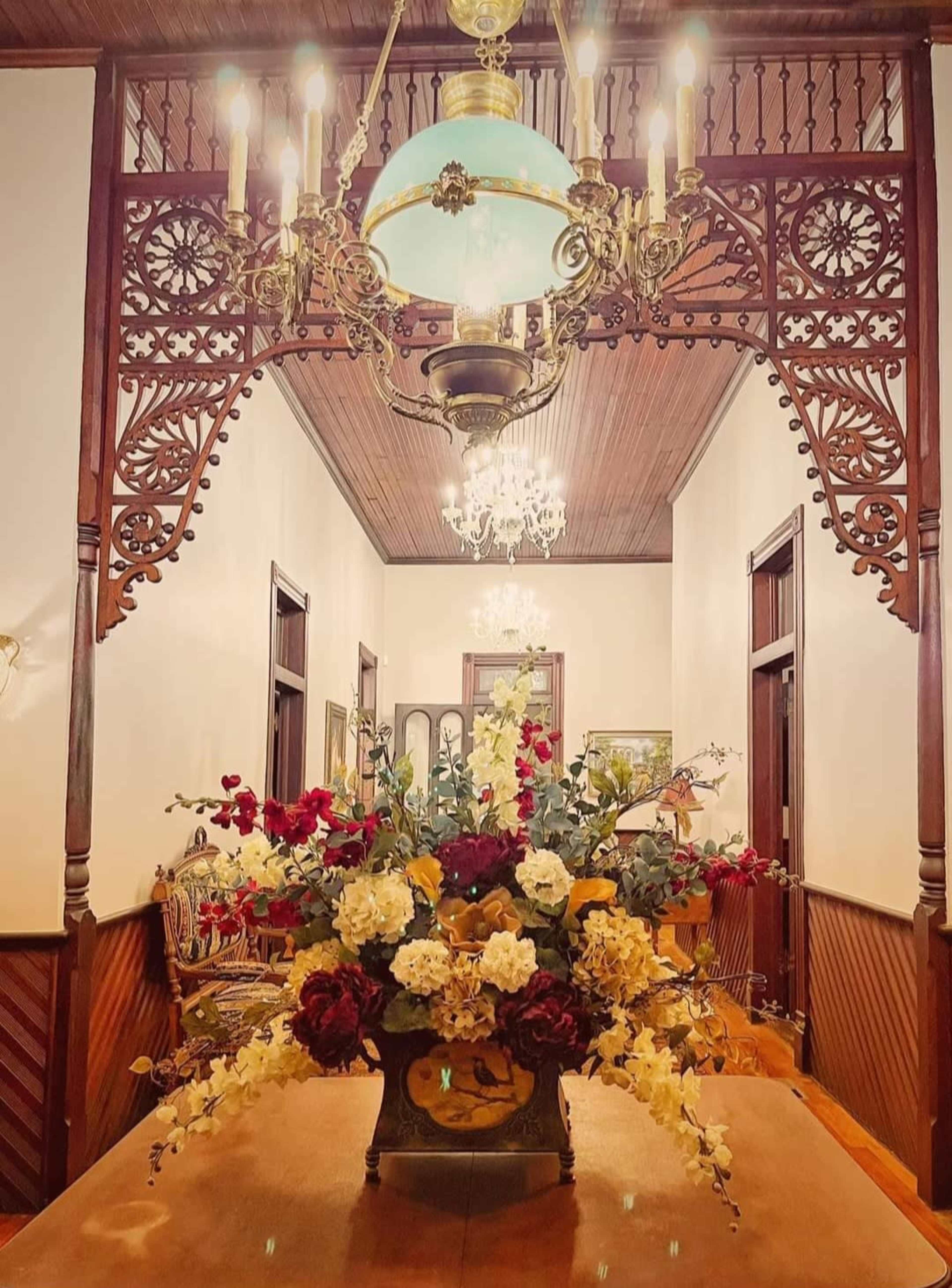 A beautifully decorated hallway with an ornate chandelier and a large floral arrangement on a wooden table.